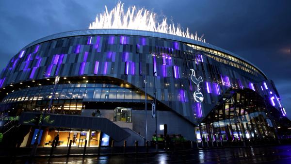 The iconic Tottenham Hotspur Stadium at night, illuminated in purple and with fireworks overhead.
