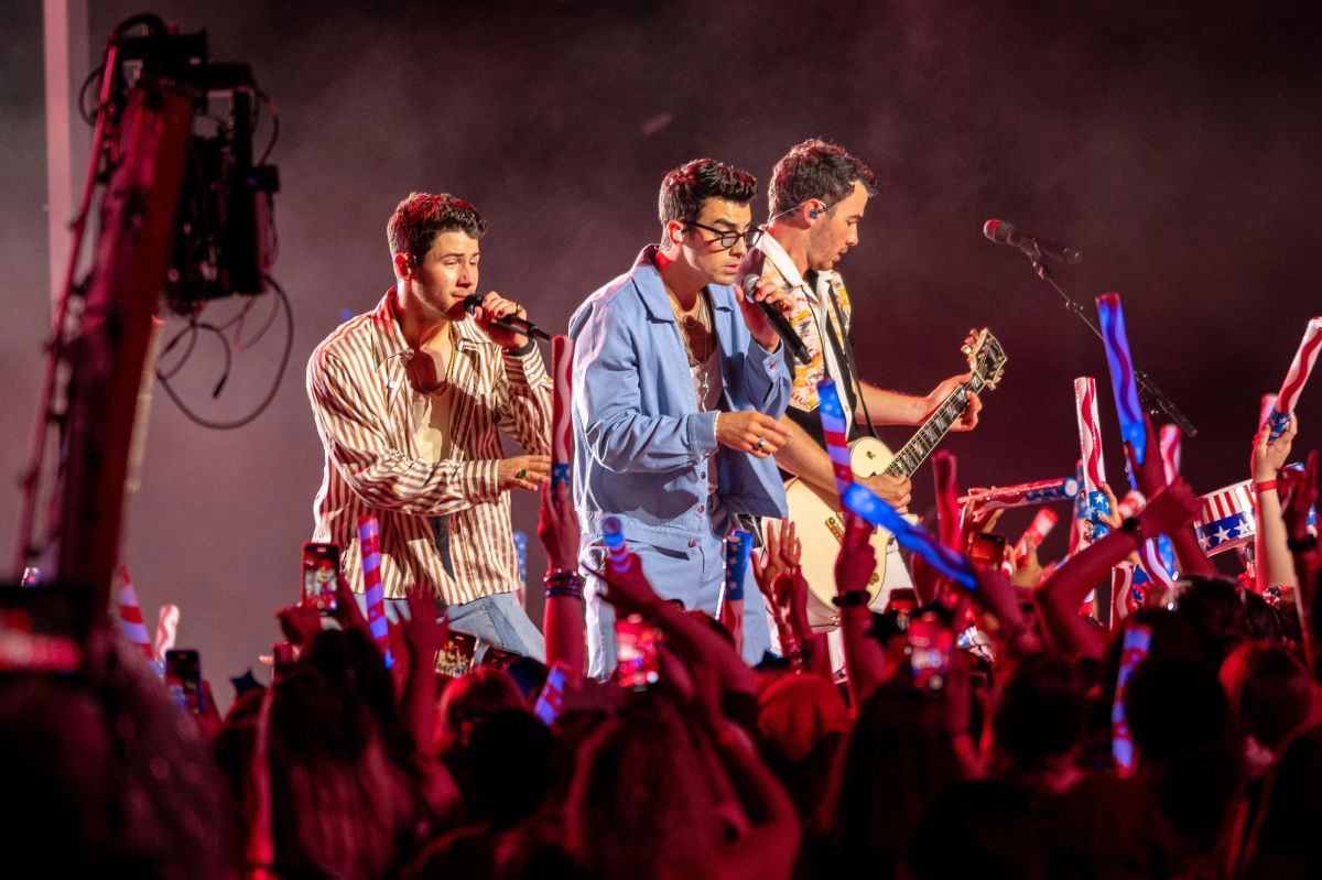 The three Jonas Brothers singing on stage above a crowd waving glow sticks