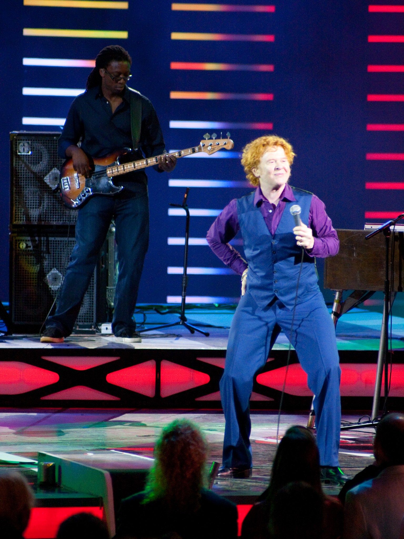 Mick Hucknall smiling and dancing on stage as the bass player performs behind him