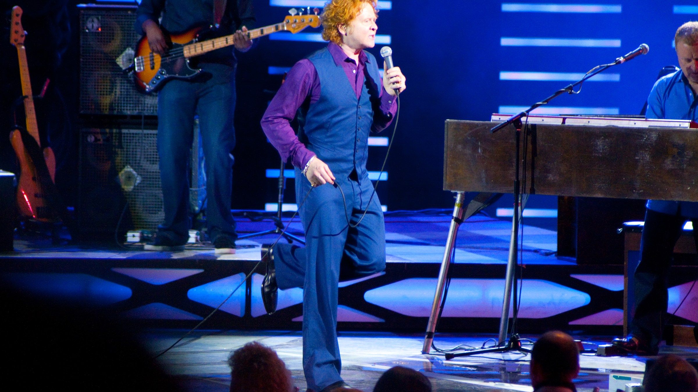 Mick Hucknall singing and dancing on a blue-lit stage between the bass player and the keyboard player