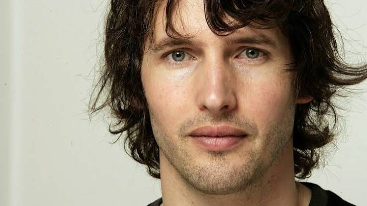 Close-up of a younger James Blunt with shoulder-length dark hair against a plain pale background