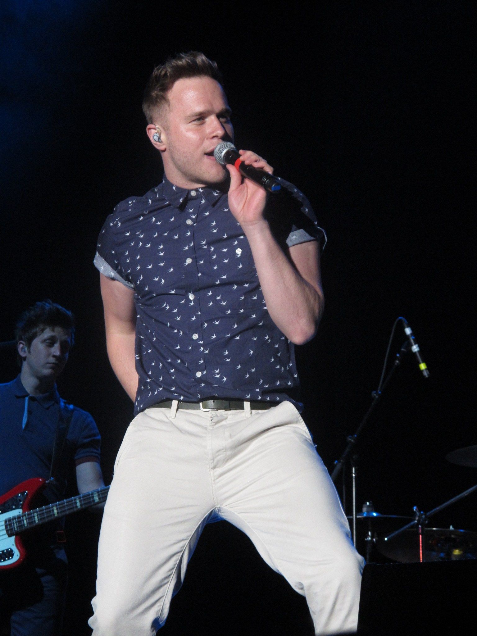Olly Murs singing on stage in a patterned short-sleeved shirt, with his bass player behind him