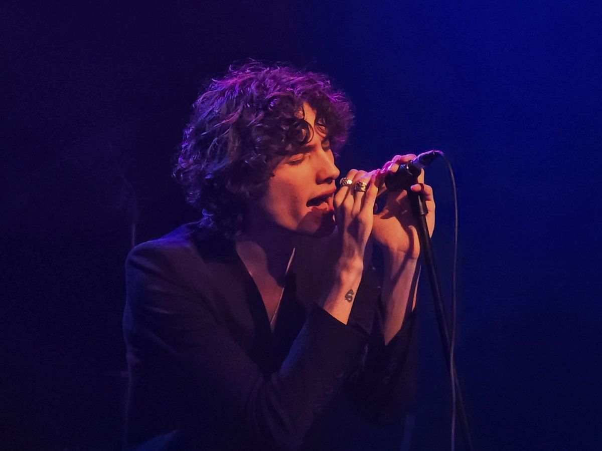 sombr singing with both hands on a microphone under purple stage light