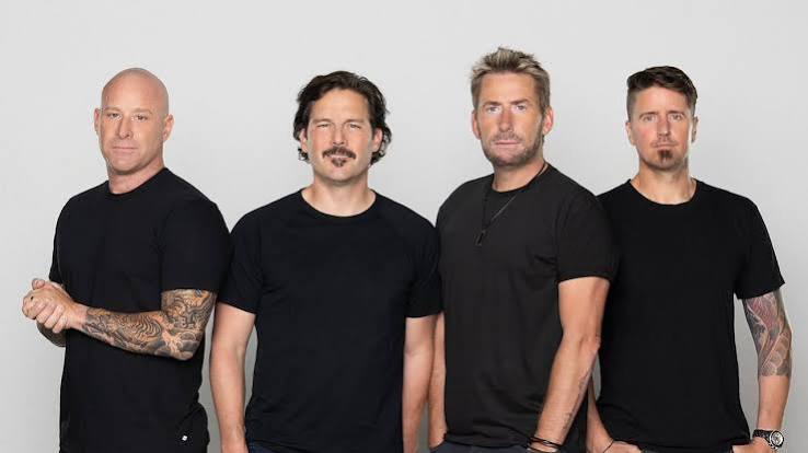 The four members of Nickelback standing in a row in black T-shirts against a light grey backdrop