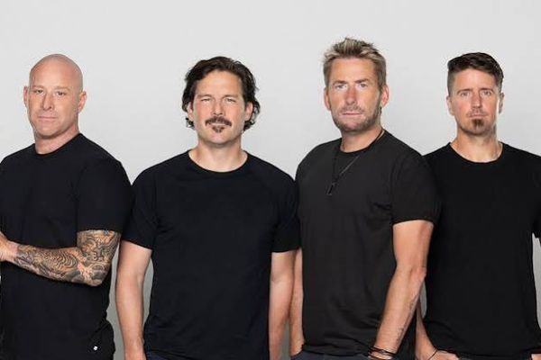 The four members of Nickelback standing in a row in black T-shirts against a light grey backdrop