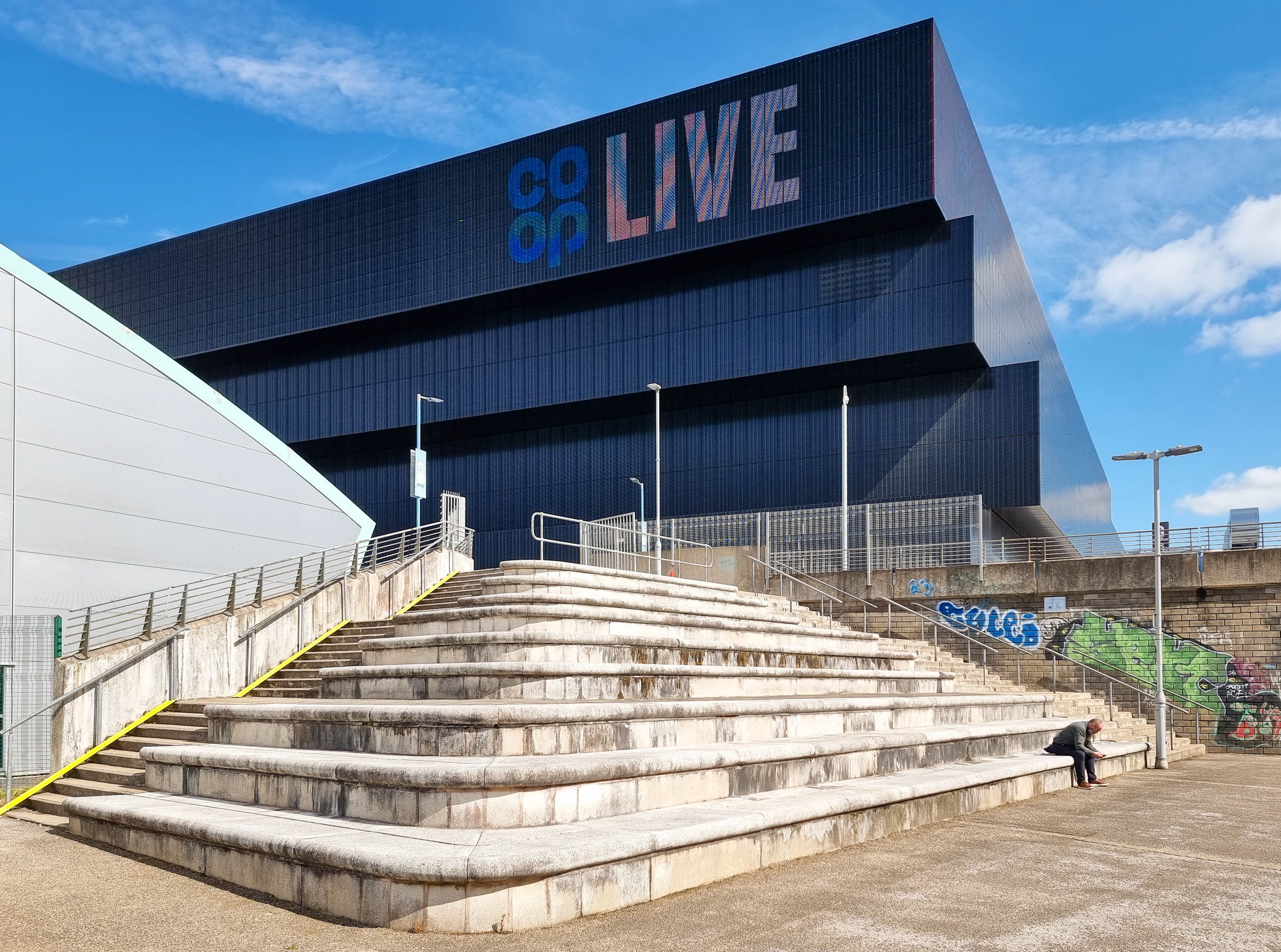 Co-op Live arena in Manchester seen from wide stone steps under a blue sky, September 2024
