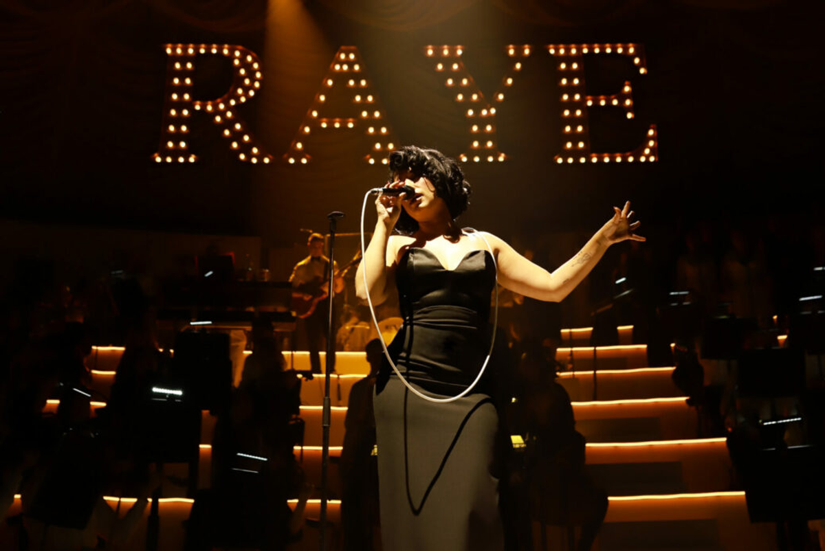 Raye performs on stage, holding a mic, with 