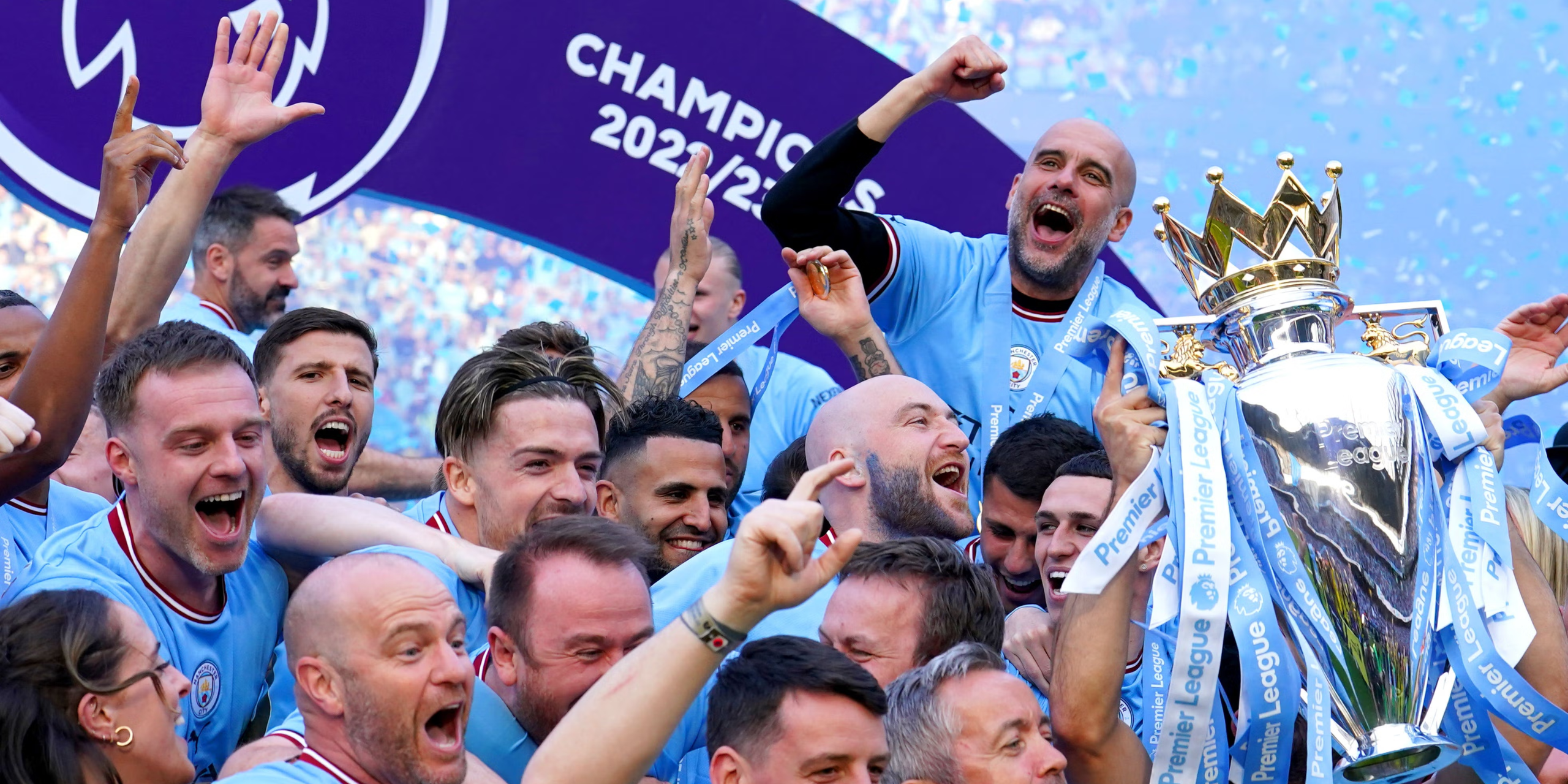 Guardiola, Grealish & Man City players joyfully lift the Premier League trophy, confetti flying.