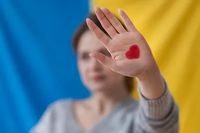 rozmyta postać kobiety na tle ukraińskiej flagi z wyciągniętą dłonią i rysunkiem serca na dłoni