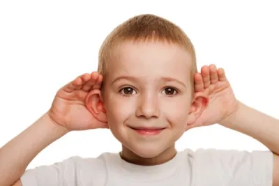 zdjęcie dziecka nadstawiającego uszy, chłopiec trzymający się za uszy, słuchający dźwięków otoczenia