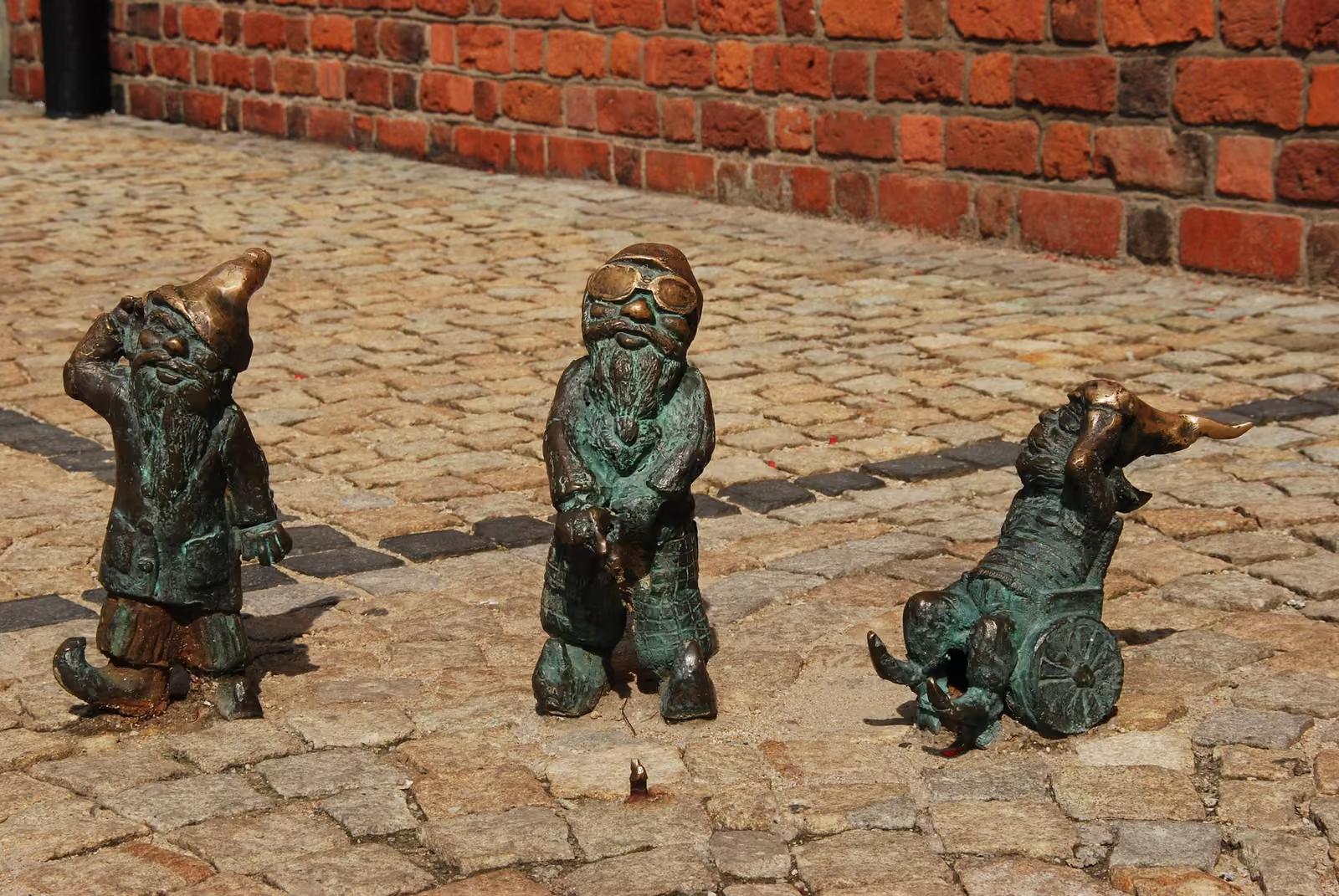 Wrocławskie krasnale z brązu na bruku przy ceglanym murze