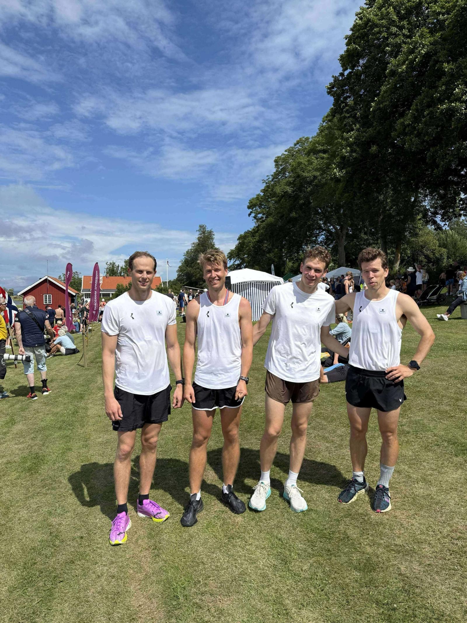 Fire venner i hvite t-skjorter med Kil Tennis & Kulturklubb-logo, ute på en sommerdag.