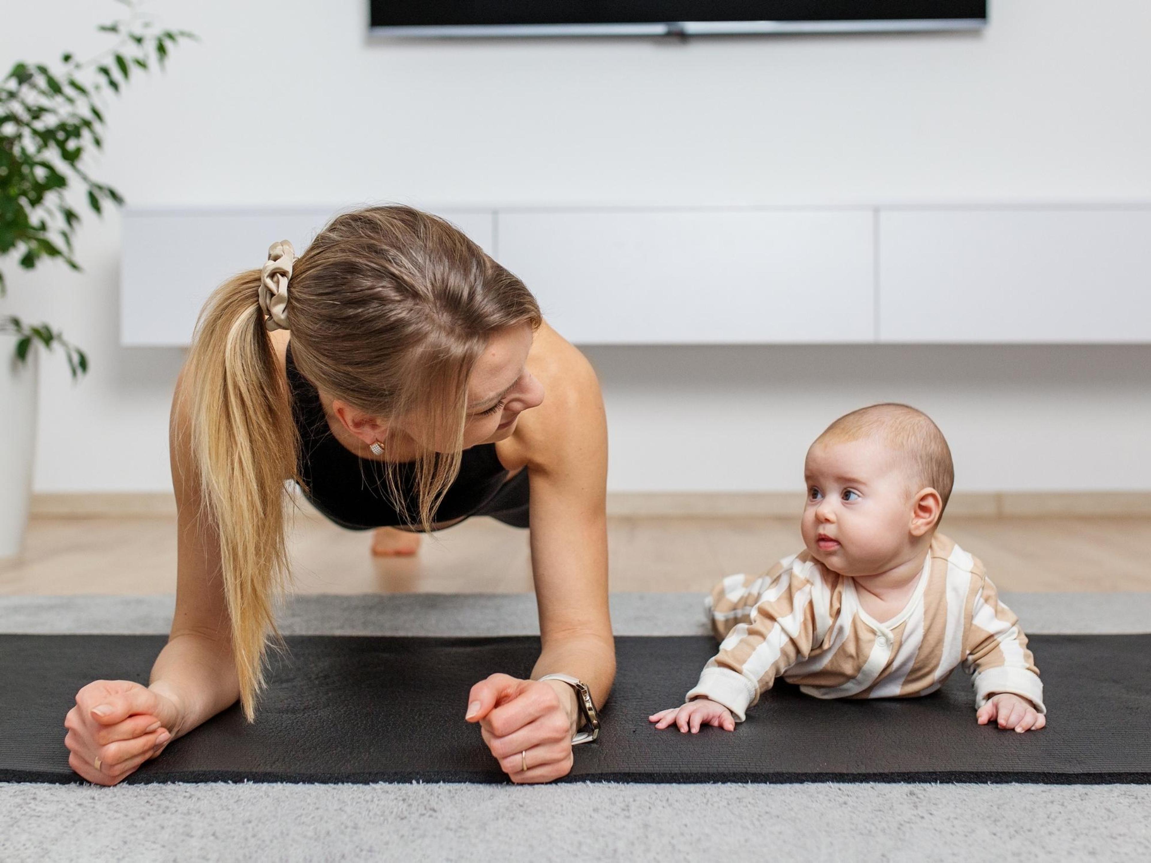 A postpartum mom doing core exercises with her baby next to her.