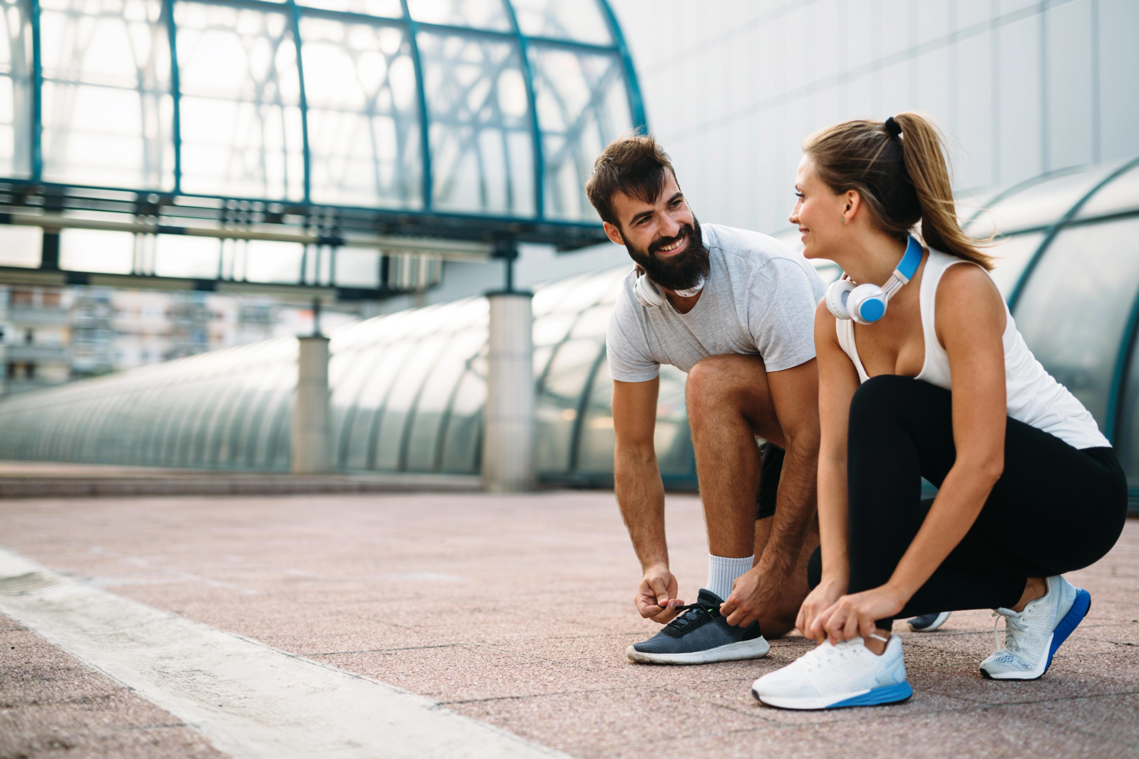 Zwei Läufer:innen bereiten sich auf das Lauftraining vor und schnüren ihre Laufschuhe