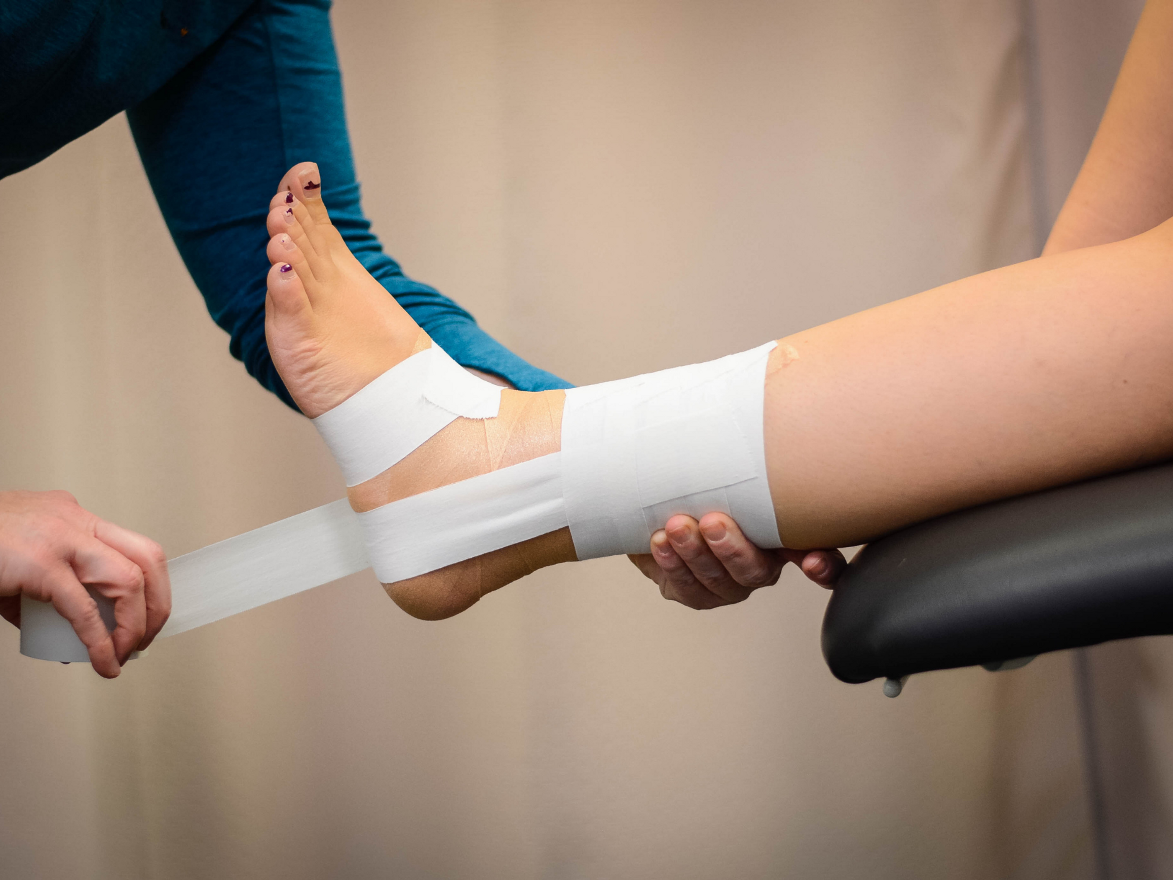 Das Umwickeln eines verstauchten Knöchels mit einem starren Zinkoxidband kann helfen, den Knöchel zu stabilisieren und eine erneute Verletzung zu verhindern.