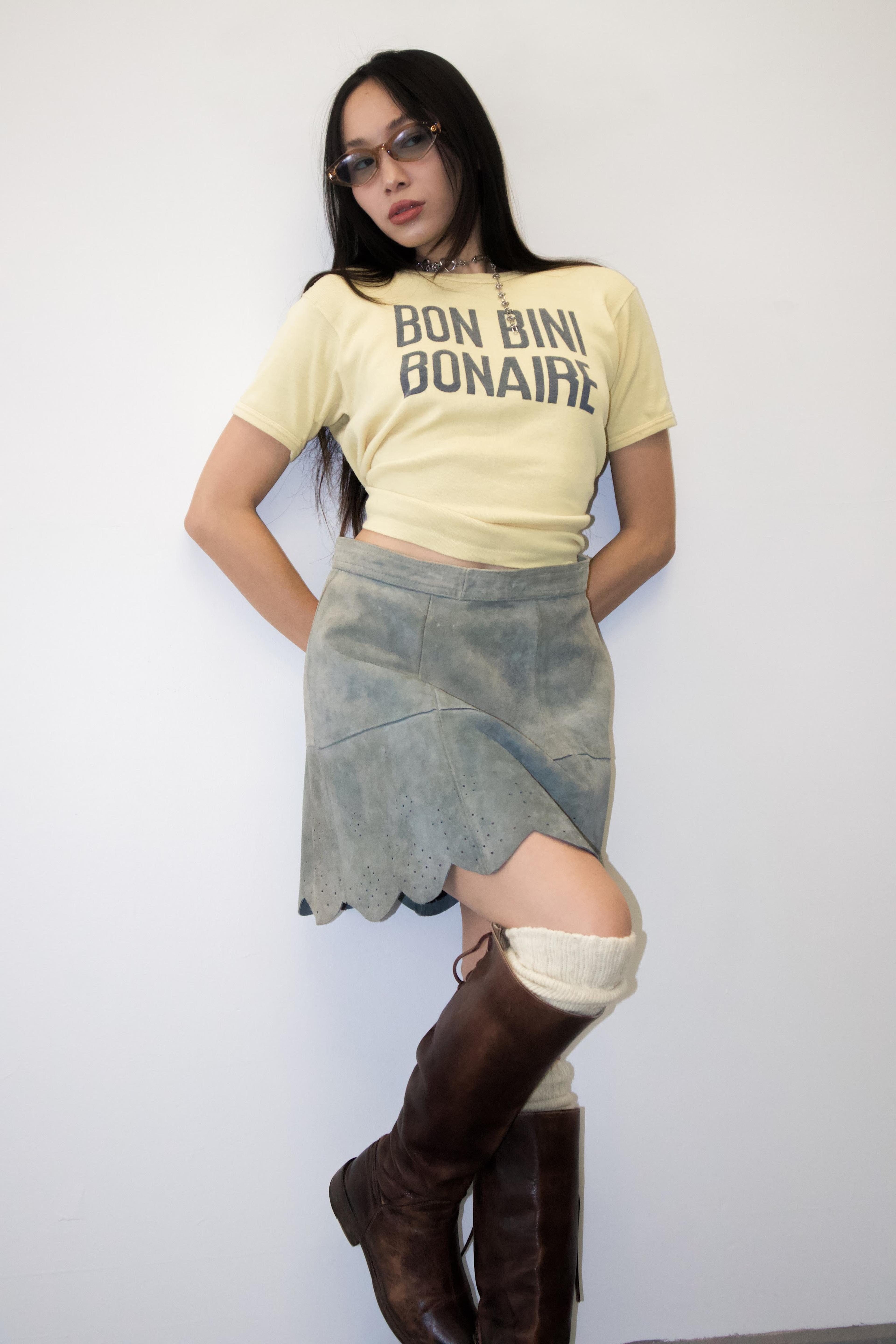 Model in a yellow graphic T-shirt, asymmetrical skirt and tall brown boots.