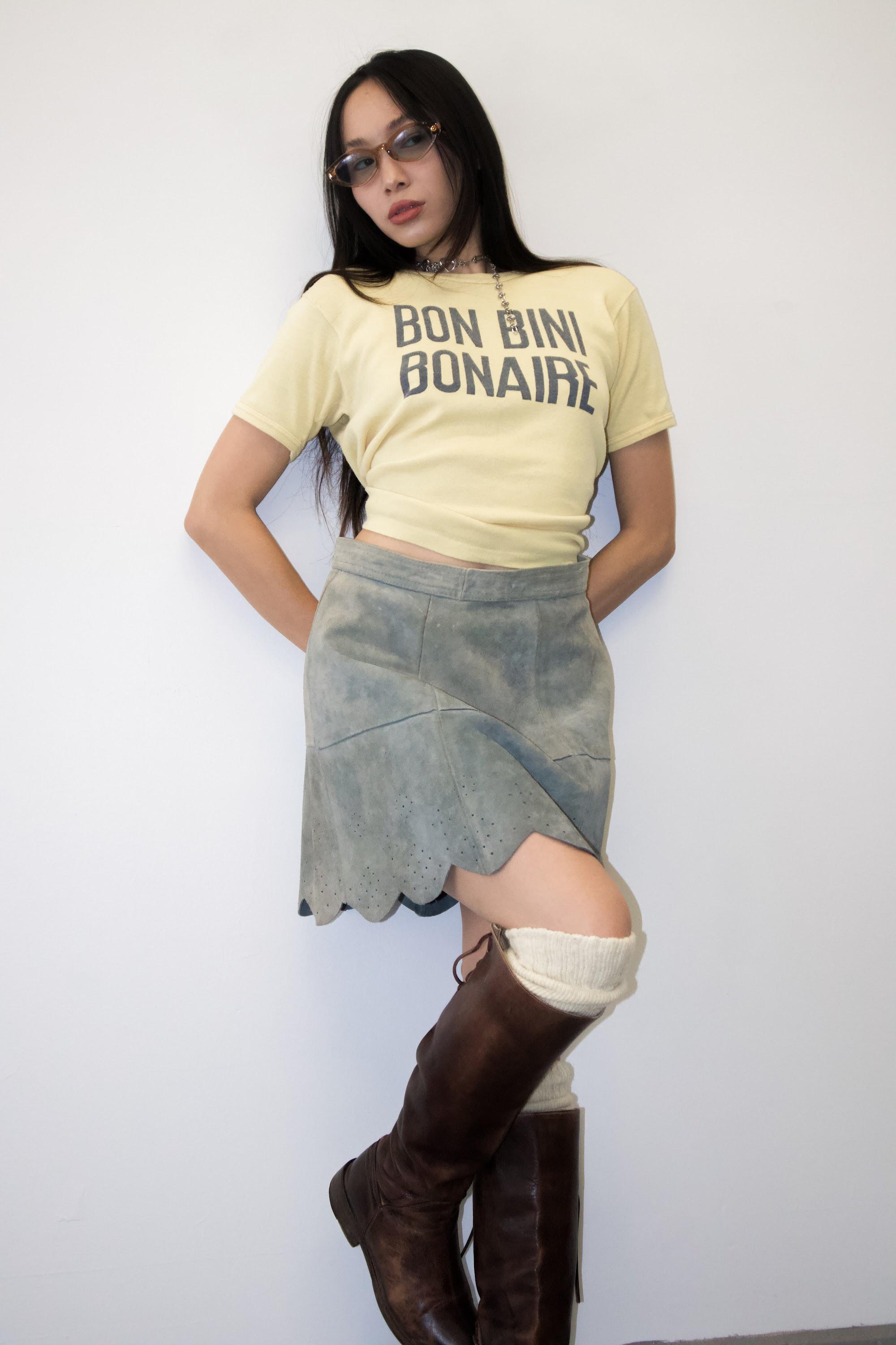 Model in a yellow graphic T-shirt, asymmetrical skirt and tall brown boots.