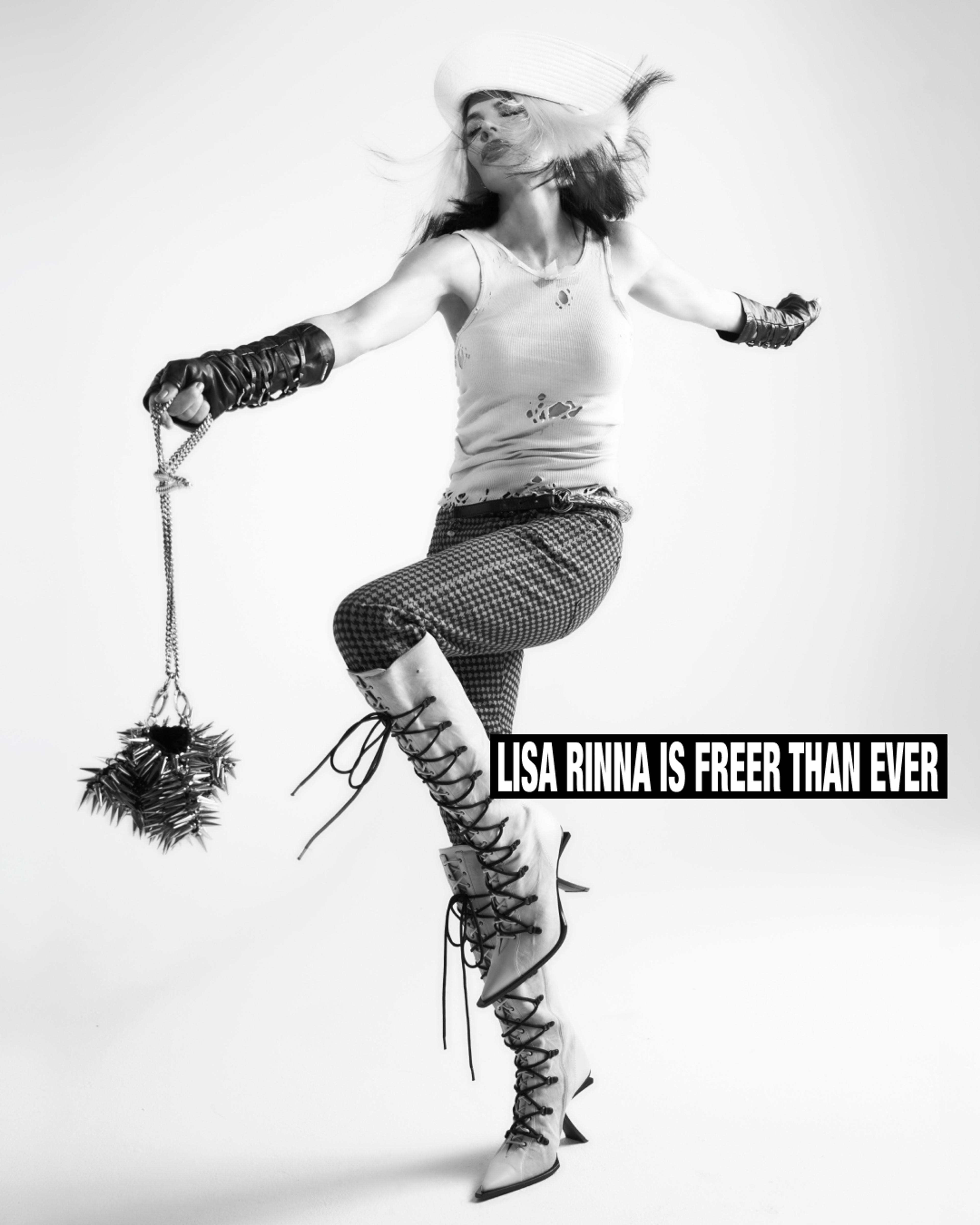 Lisa Rina in black and white wearing white boots and a sailor hat kicking in the air.