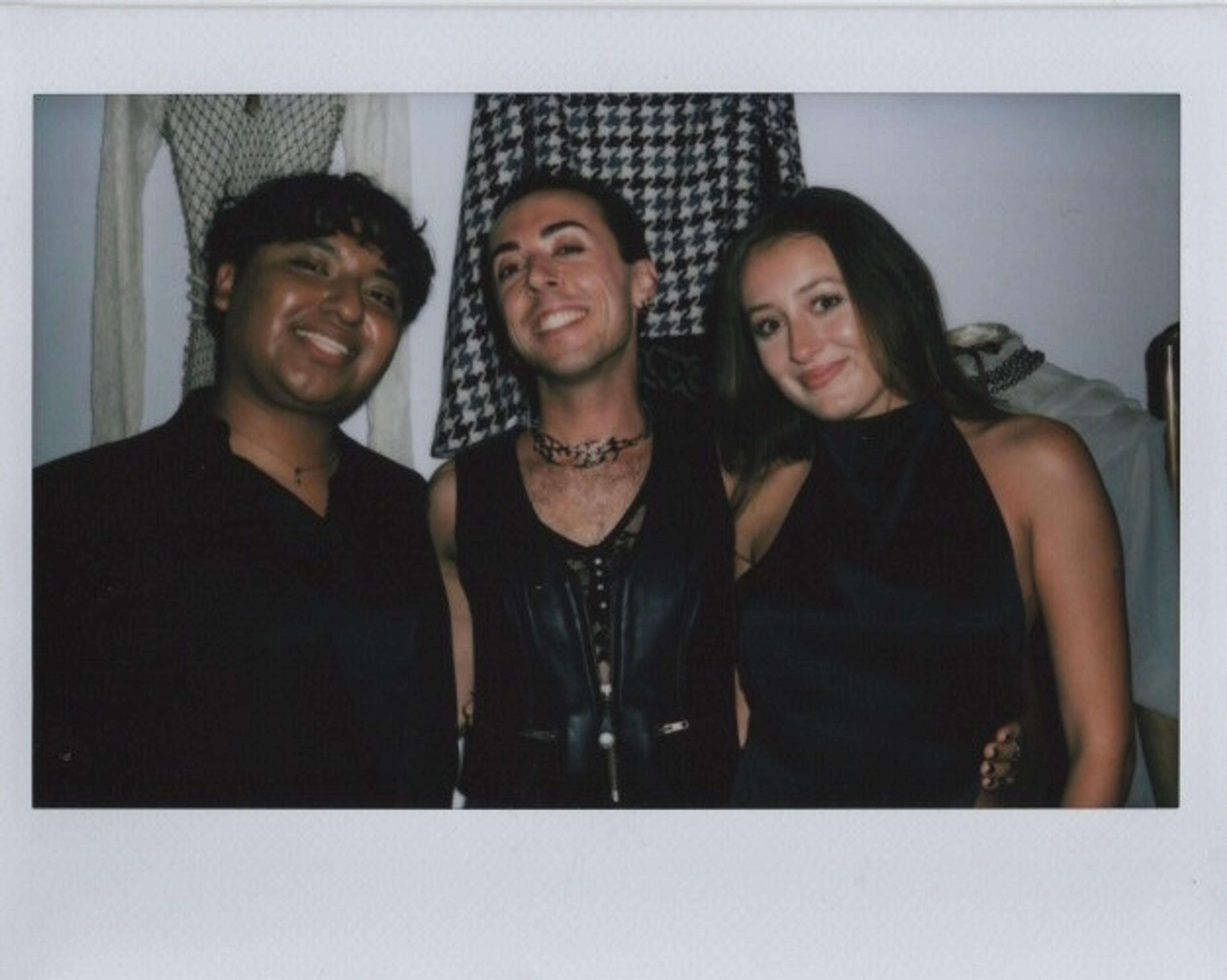Polaroid scan of three people wearing all black smiling at a party.