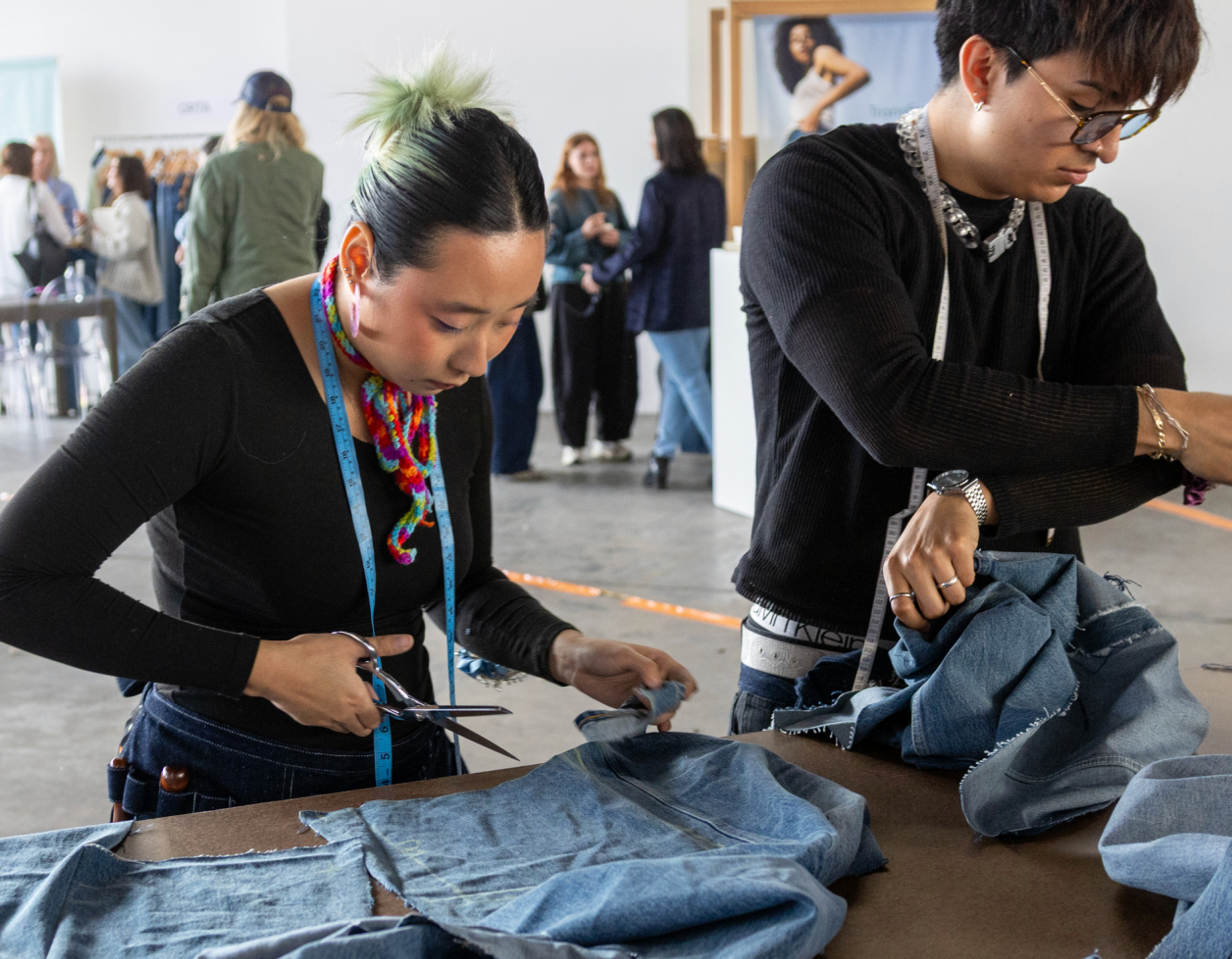 Two students cutting fabric on a work table.