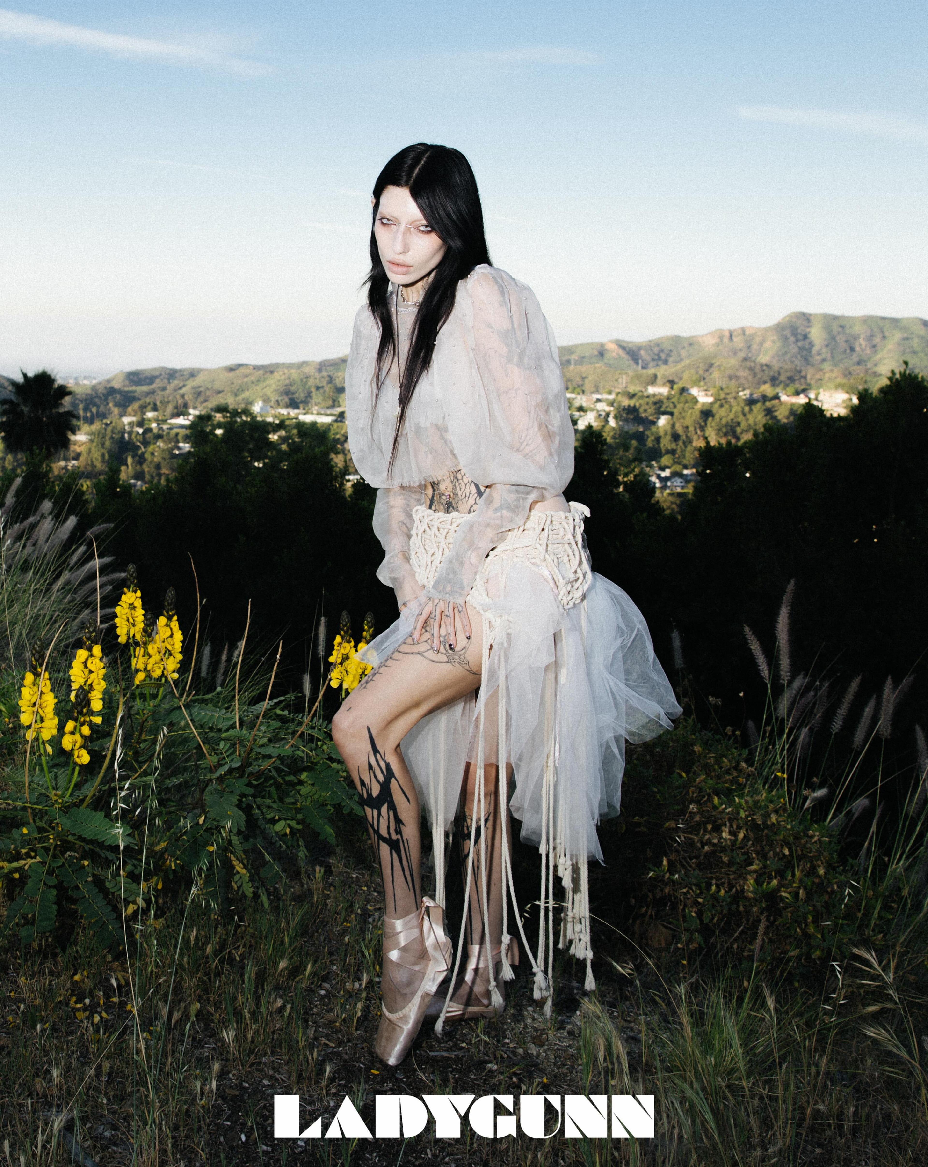 DeathByRomy wearing a layered cream look in a grassy field.