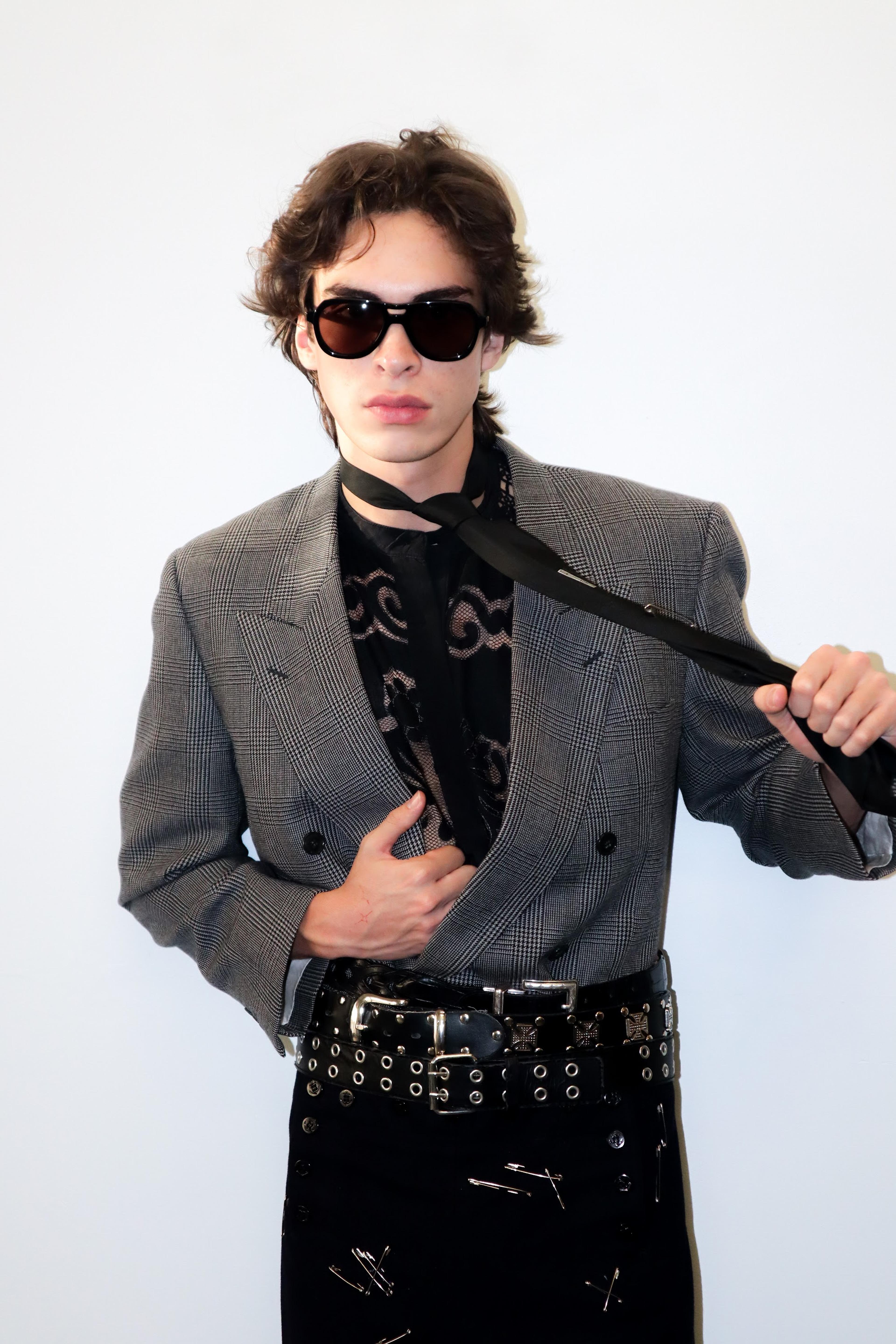 Model in a grey jacket, patterned black shirt and sunglasses.