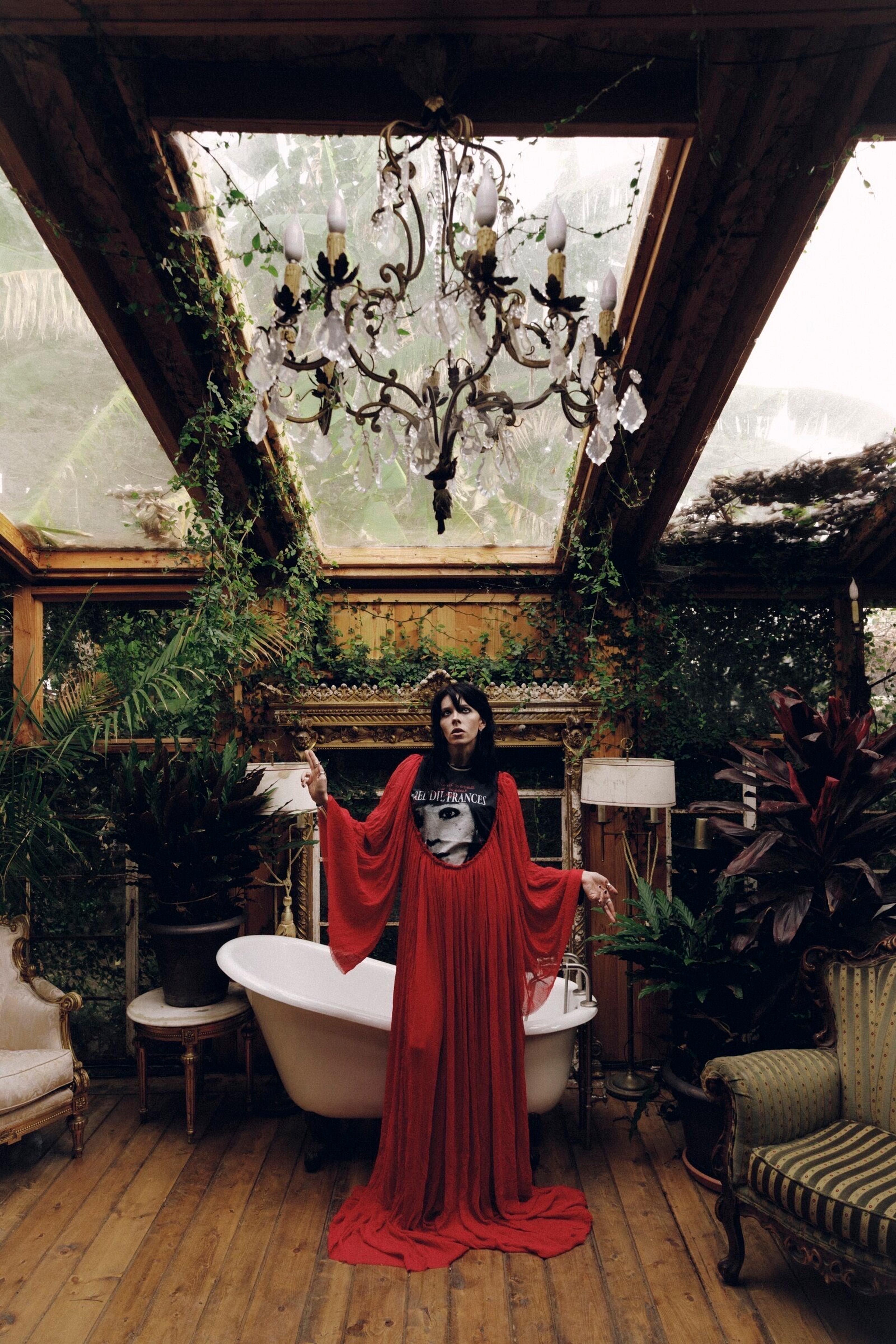 A flowing red garment beneath a chandelier in an overgrown greenhouse.