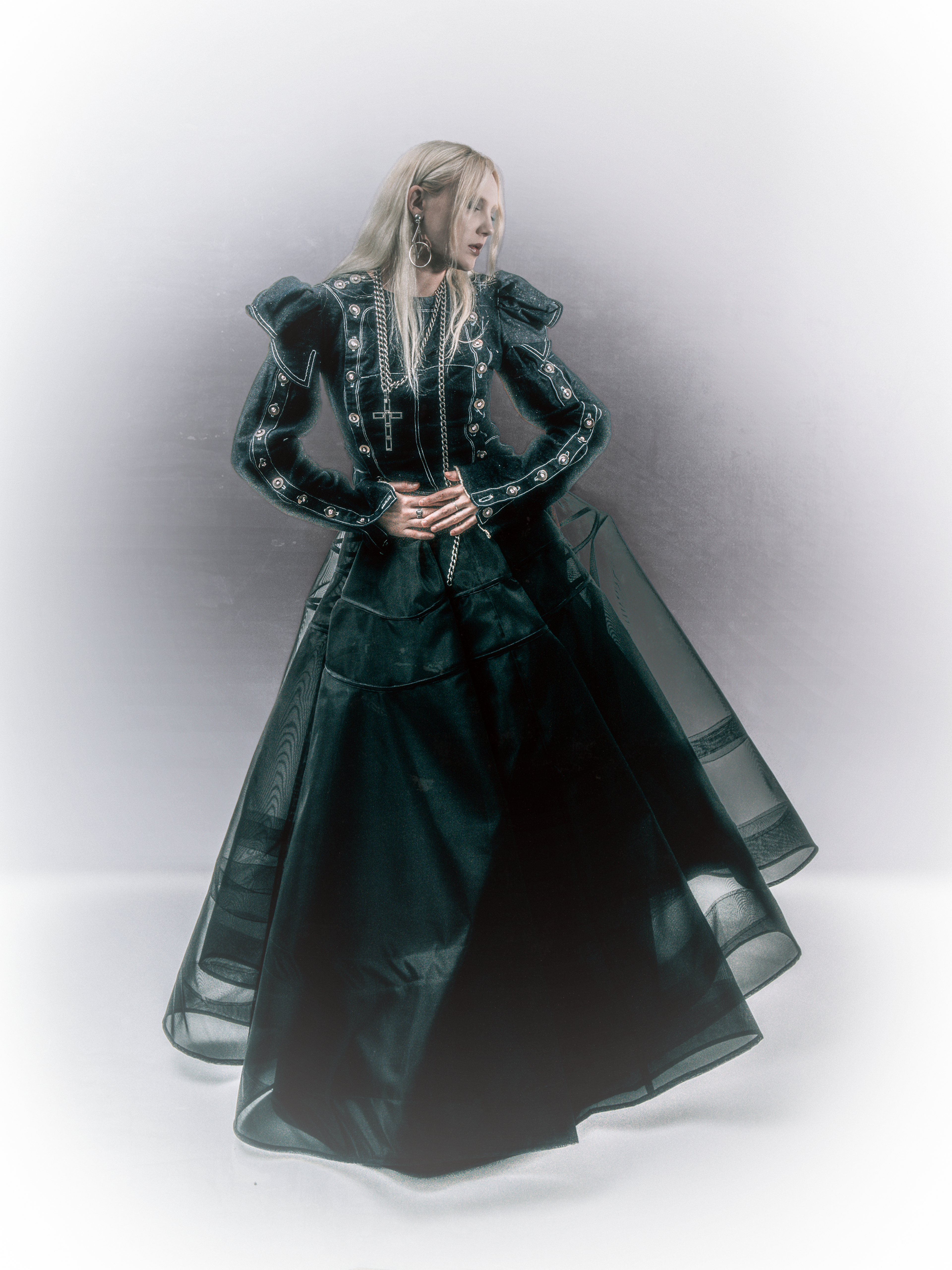 Girl wearing a big black sheer skirt and armored jacket with a metal cross belt chain.