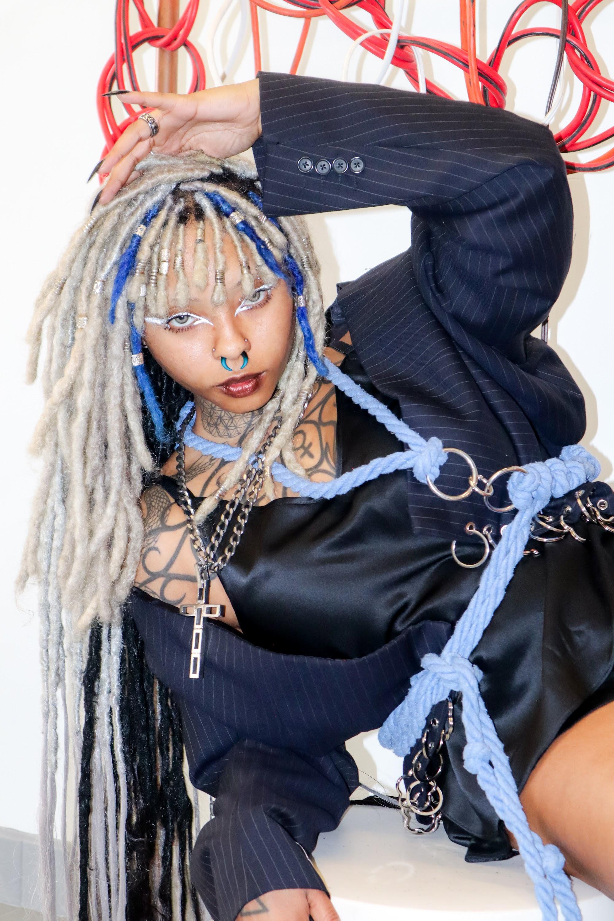 Model with pale blue braids in a pinstripe suit and layered accessories.