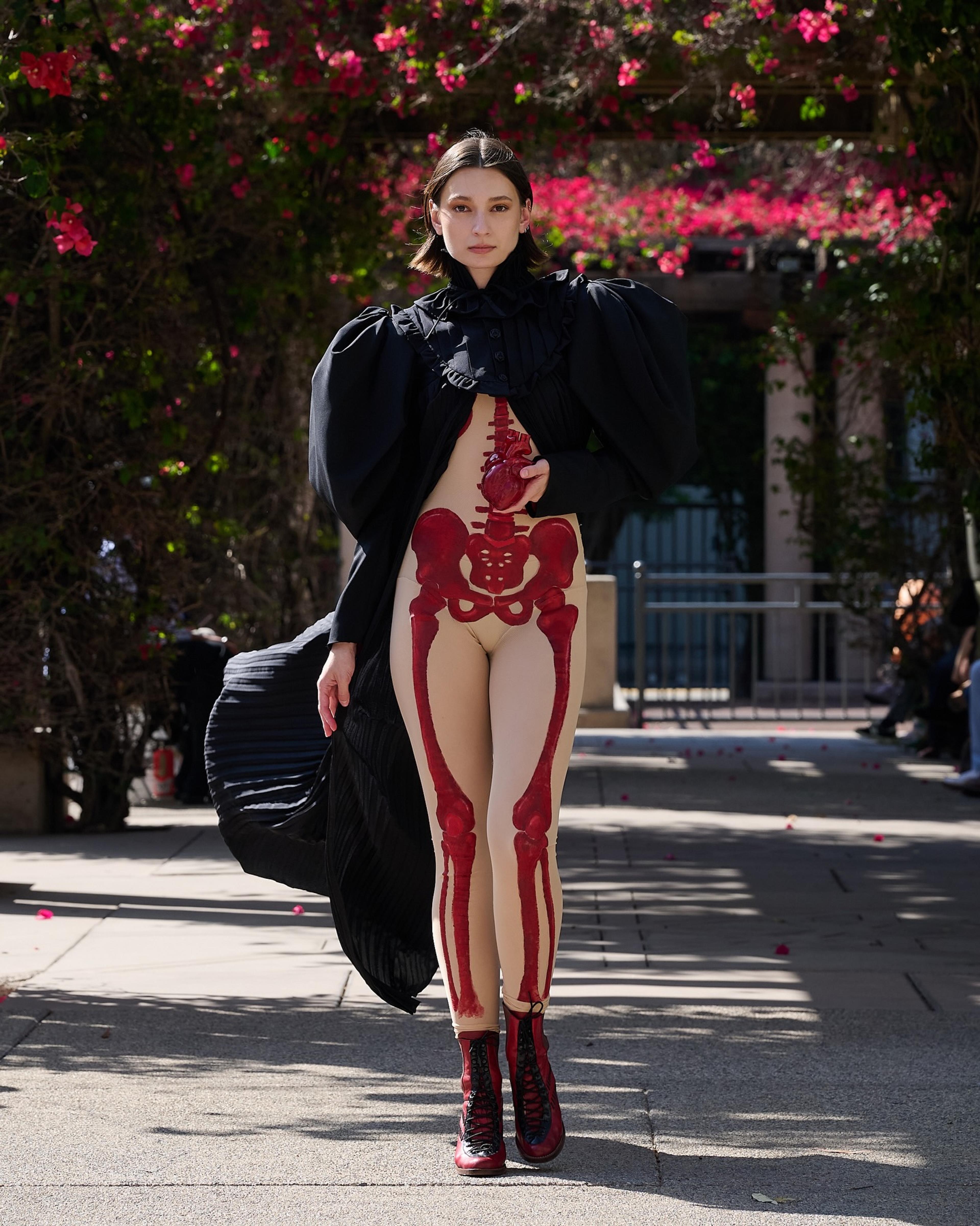 Girl in red skeleton painted jumpsuit walking runway with black coat.