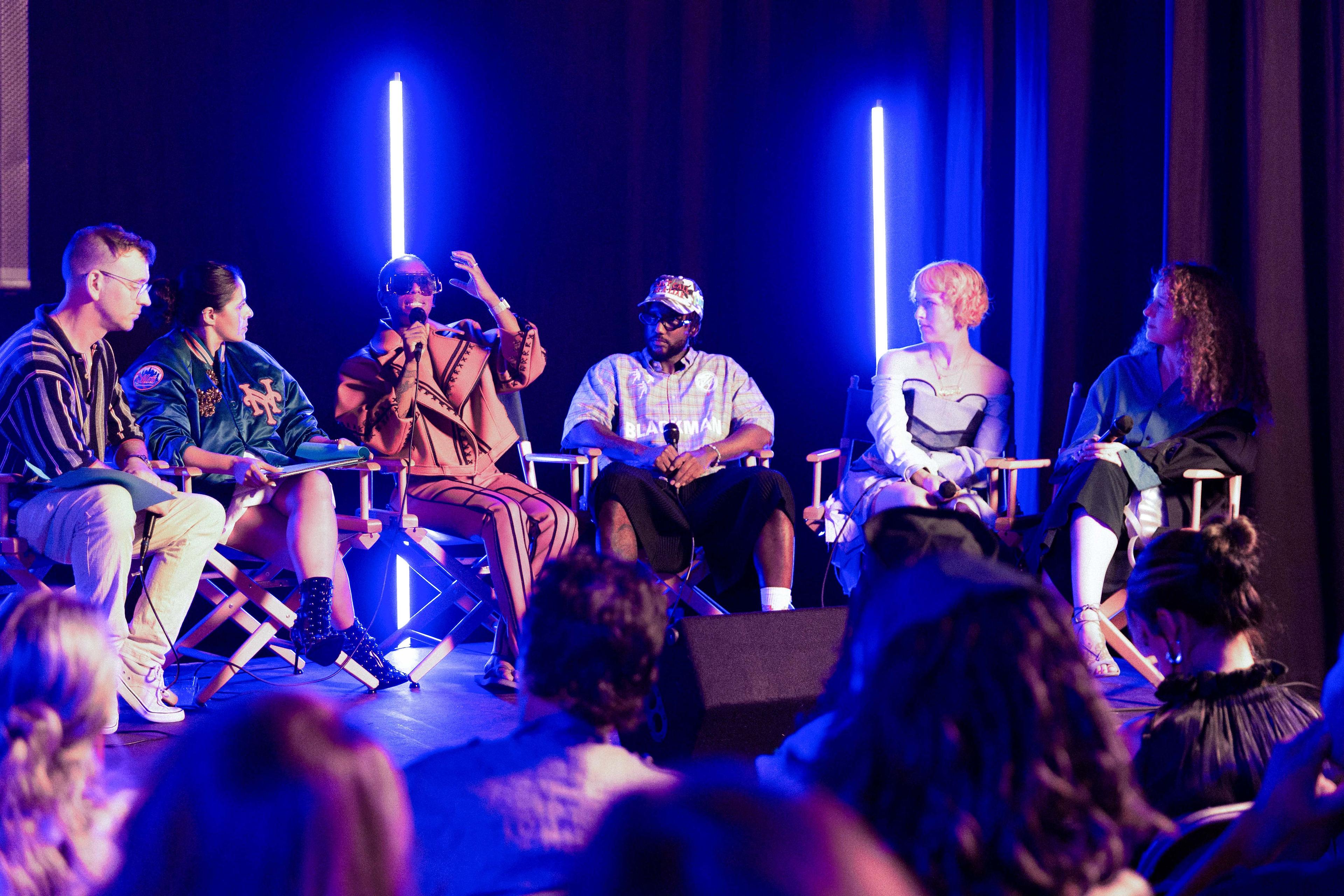Blue light panel talk on stage with six professionals talking.