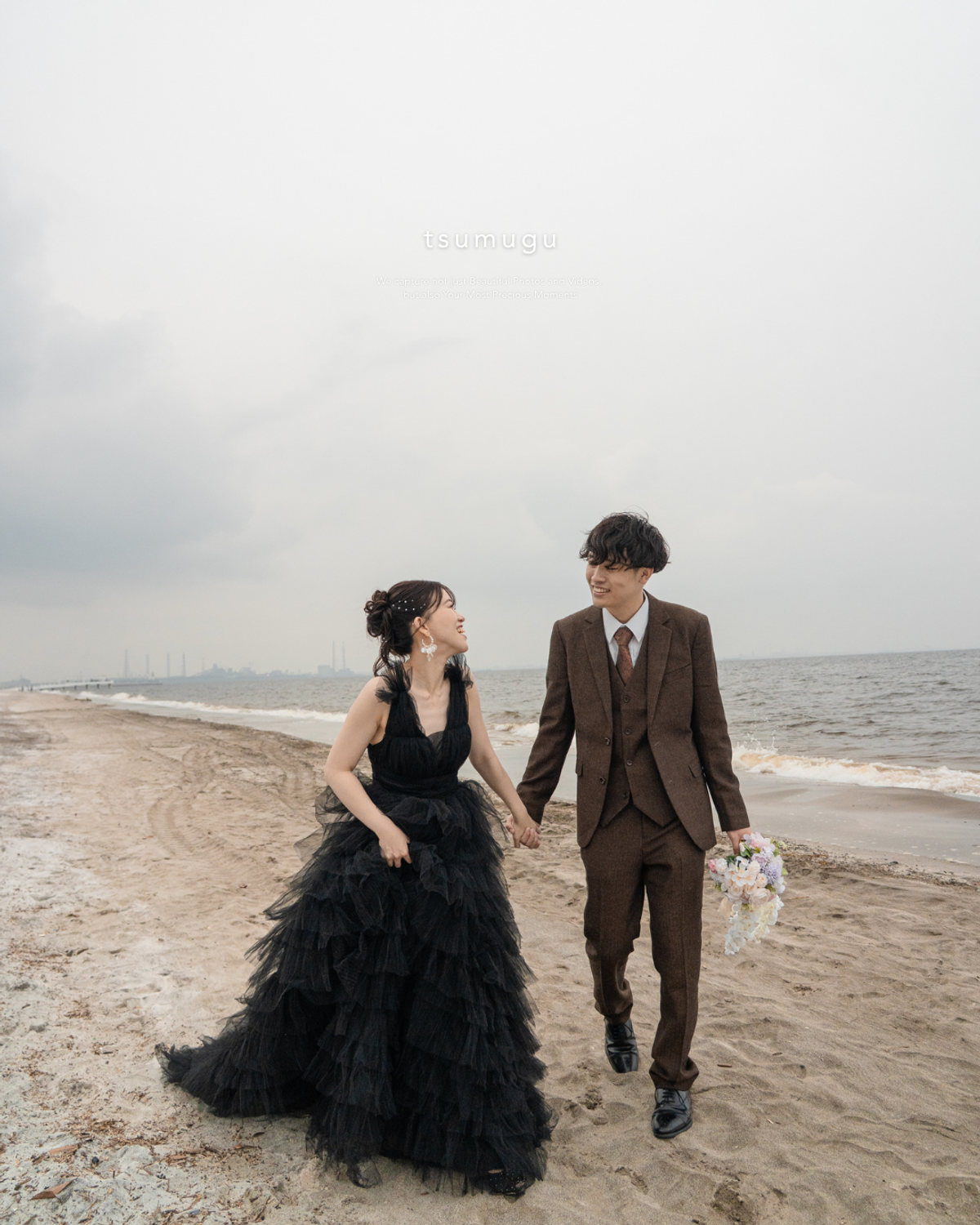 稲毛海浜公園の海辺を黒いドレスとスーツ姿で歩くふたり