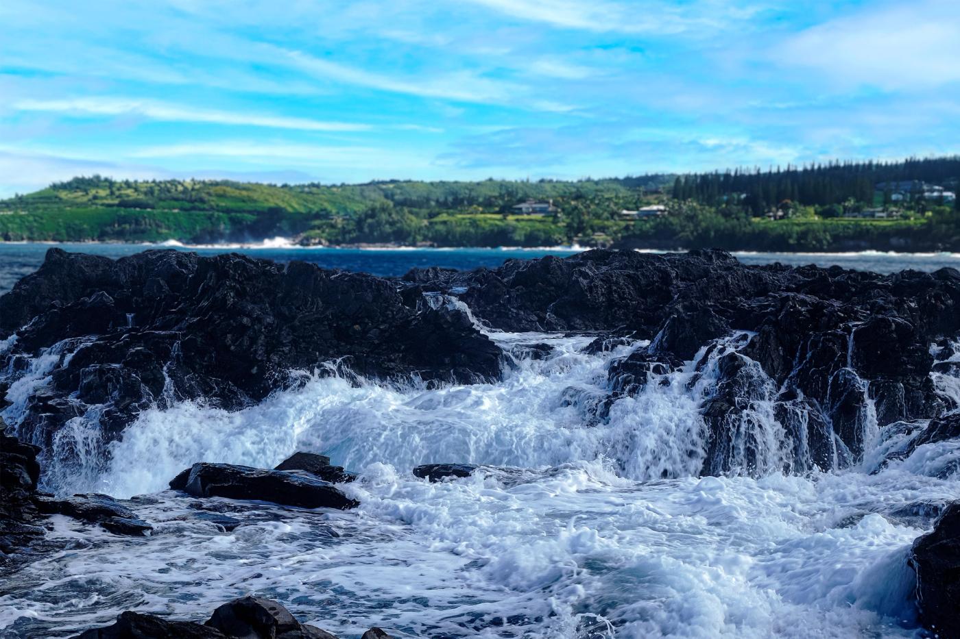 Wave crashing over lava rocks creating a waterfall