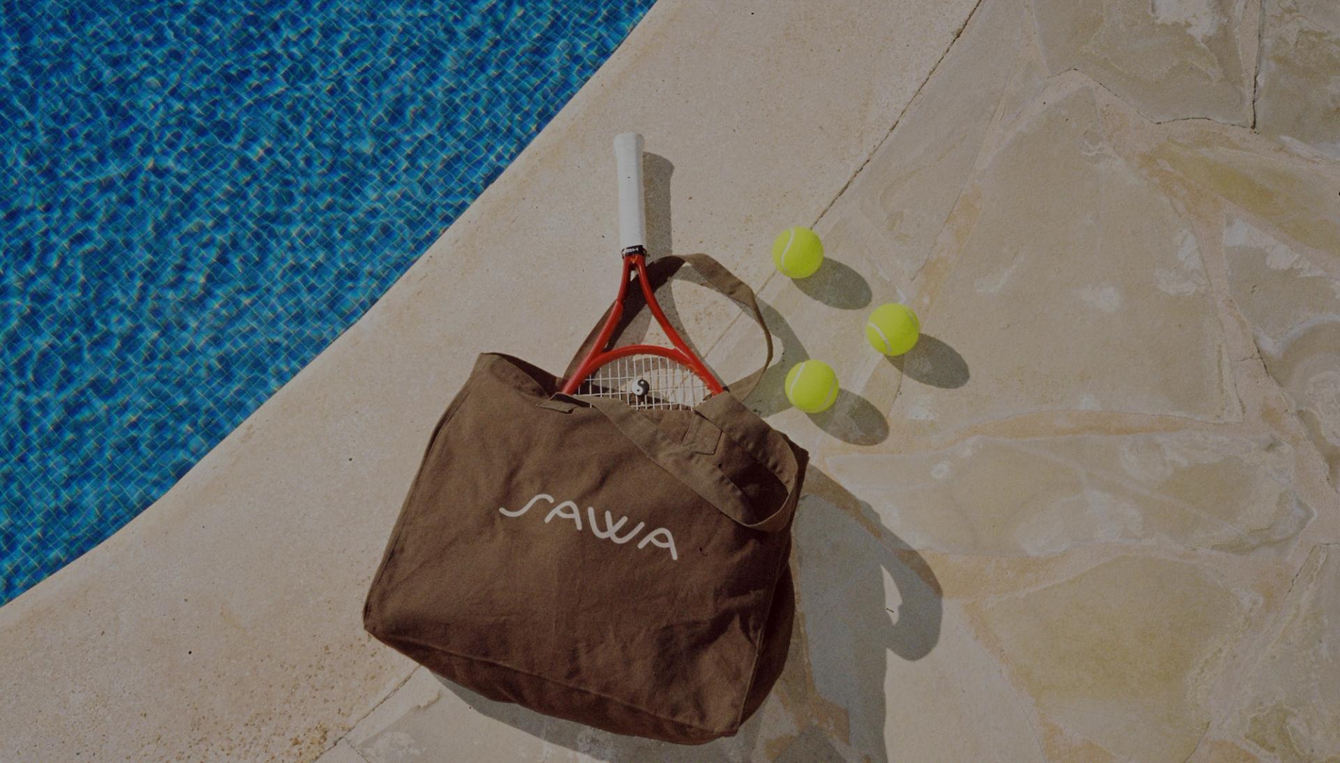 A SAWA tote bag with a tennis racket and balls beside a pool