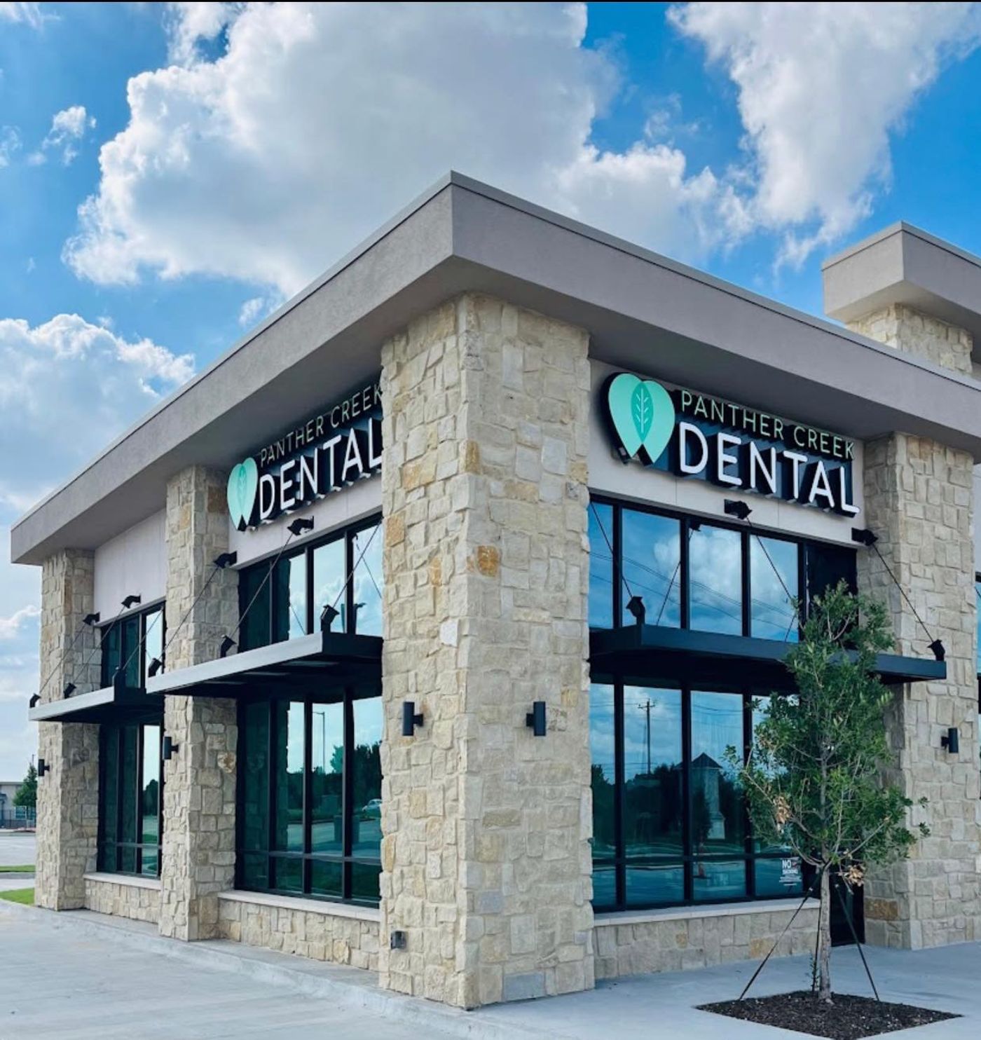 Stone and glass building exterior with illuminated Panther Creek Dental signage in Frisco, TX