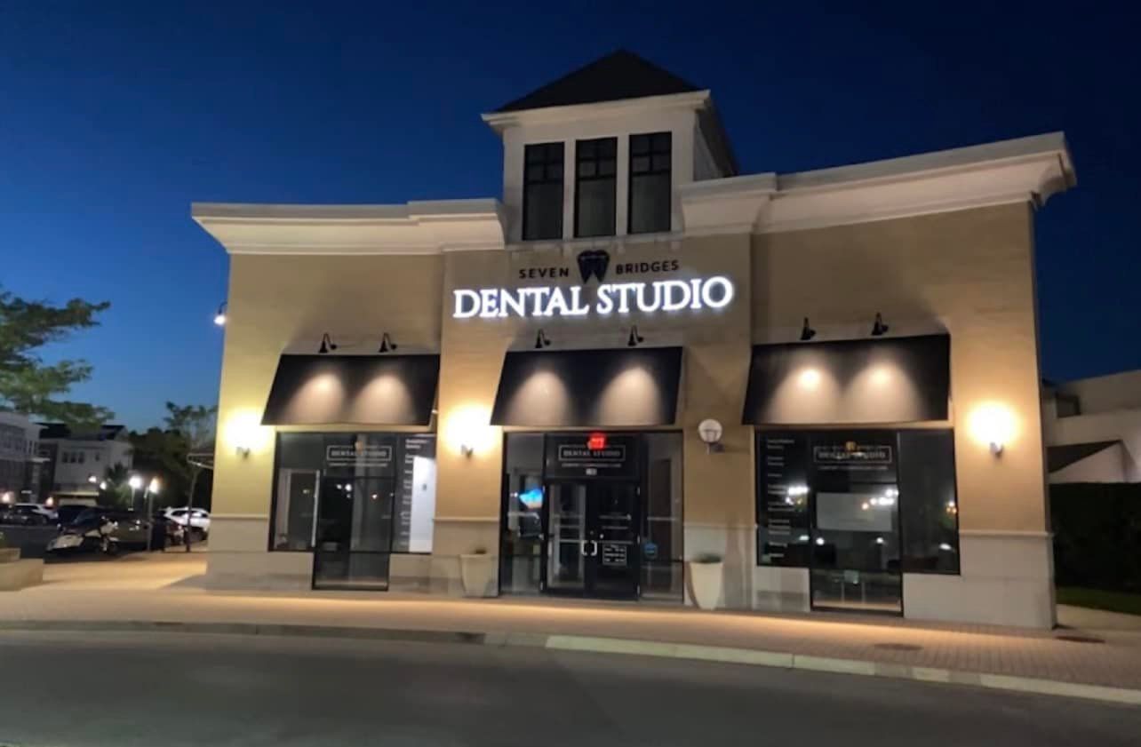 Illuminated Seven Bridges Dental Studio sign on the storefront at dusk in Woodridge, IL