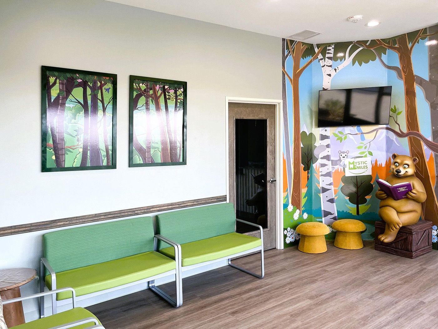 Waiting area with a forest mural, green seating and a bear statue at Mystic Smiles in Carrollton, TX