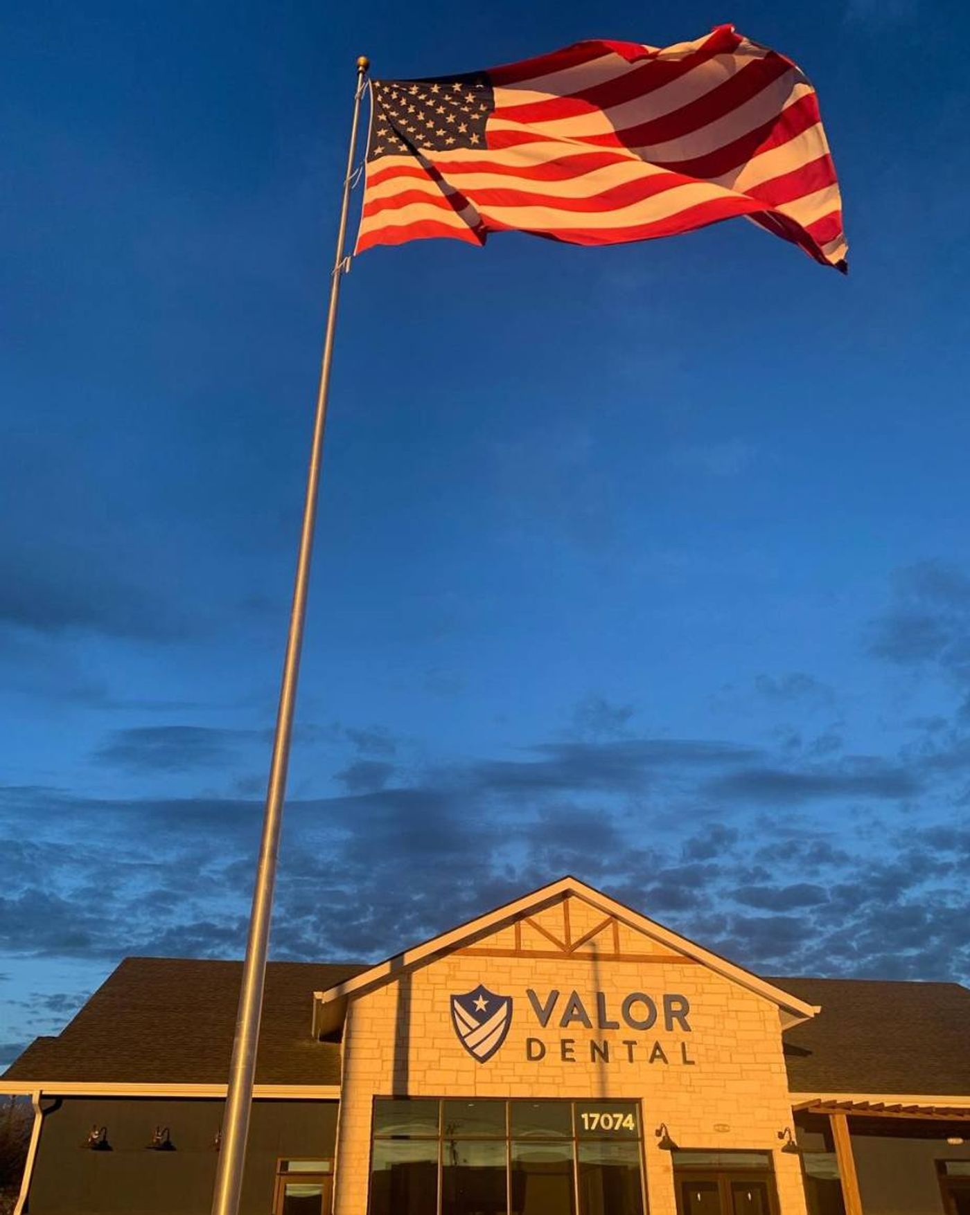 Valor Dental building sign at dusk beneath an American flag in Justin, TX