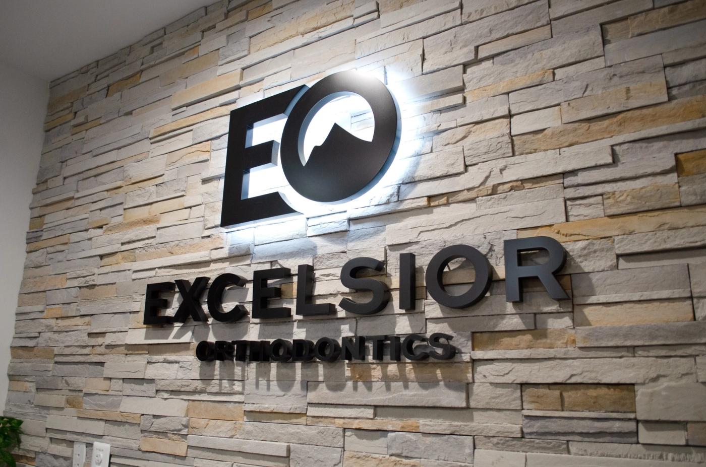 Backlit EO logo and Excelsior Orthodontics lettering on a stone wall in Purcellville, VA
