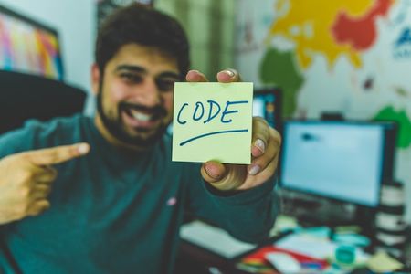 man smiling pointing at Post-it note that has the word "code" written on it