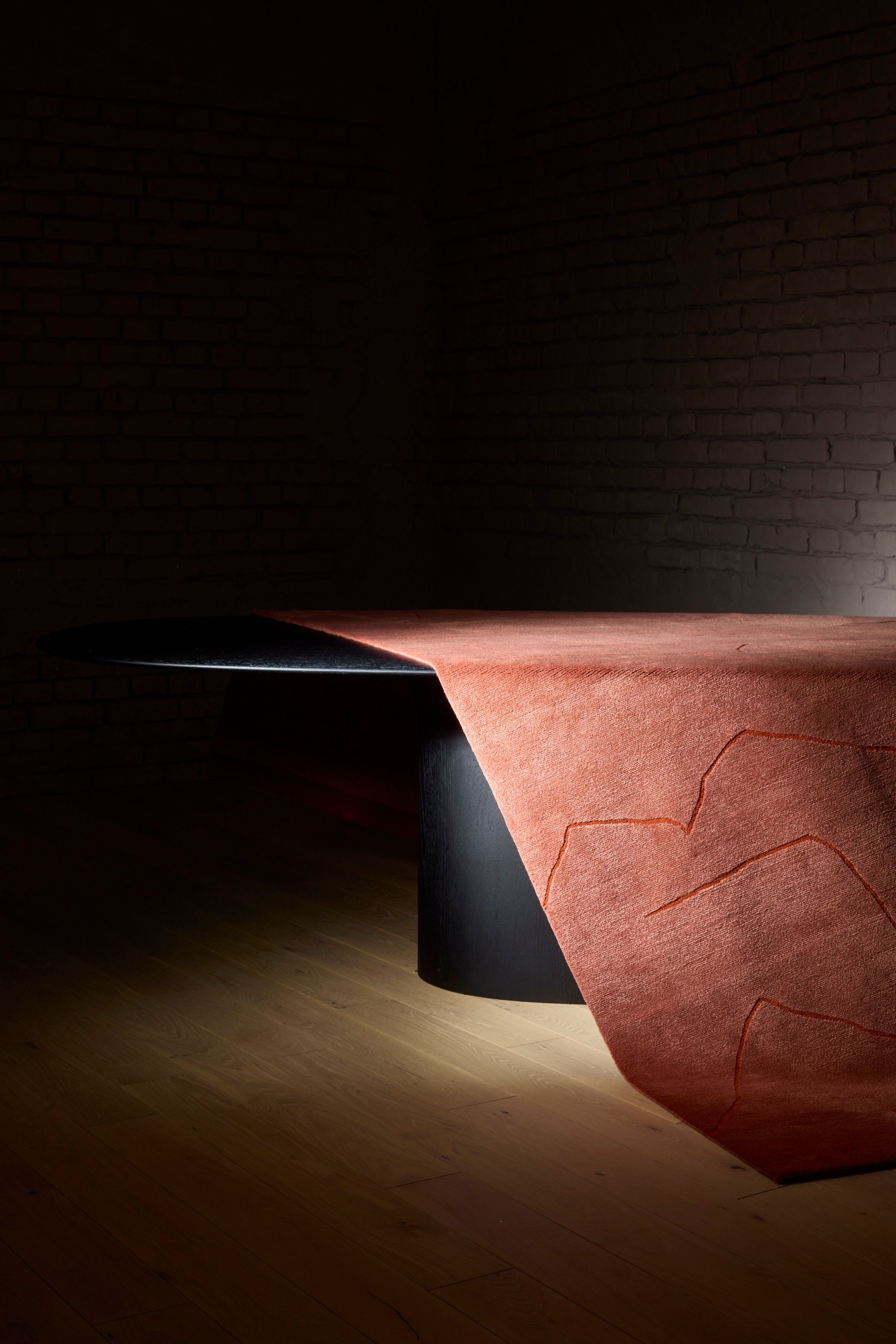 A dark space with a black table, a red rug hanging over the table
