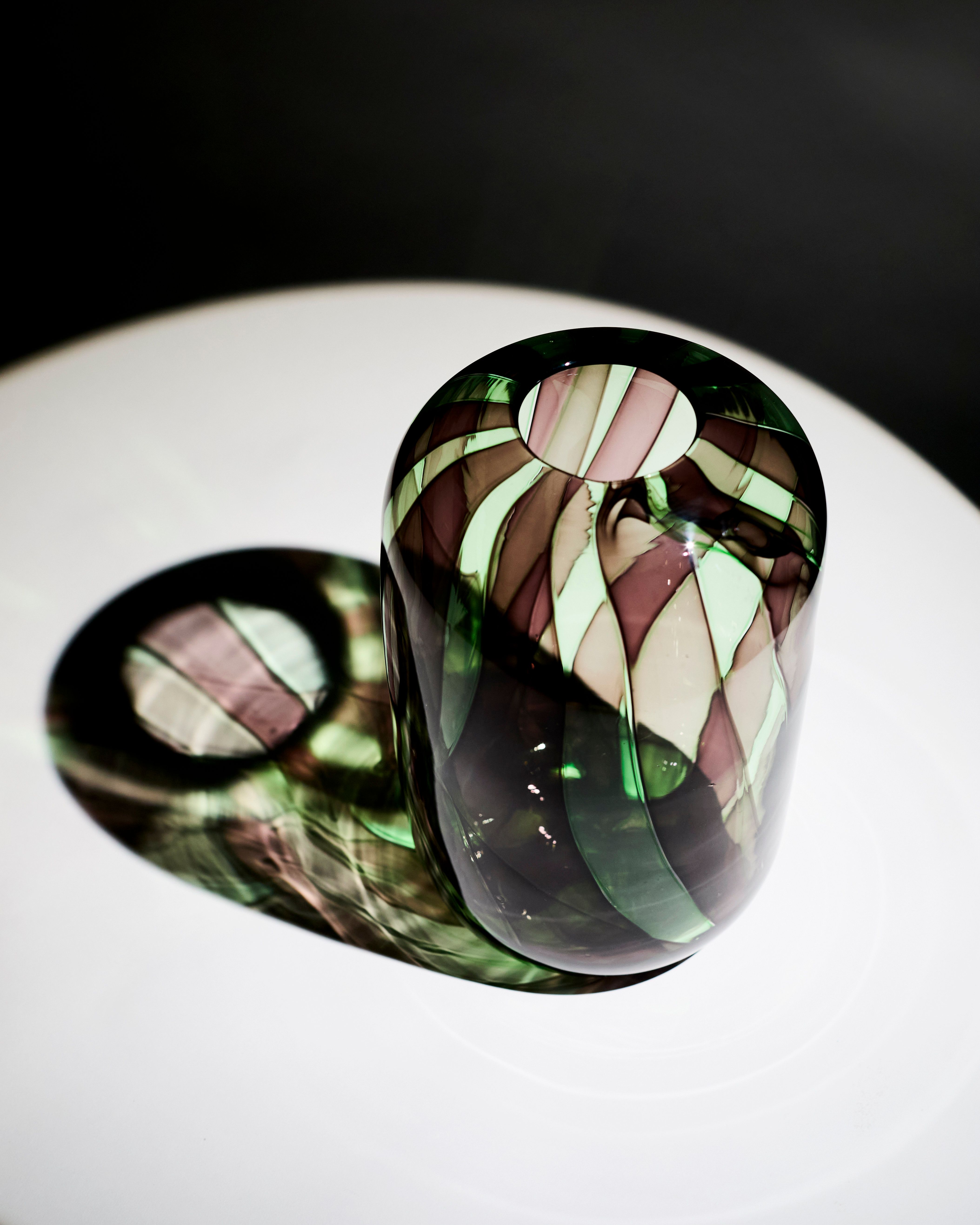 a colorful striped glass vase casting a shadow on a white table