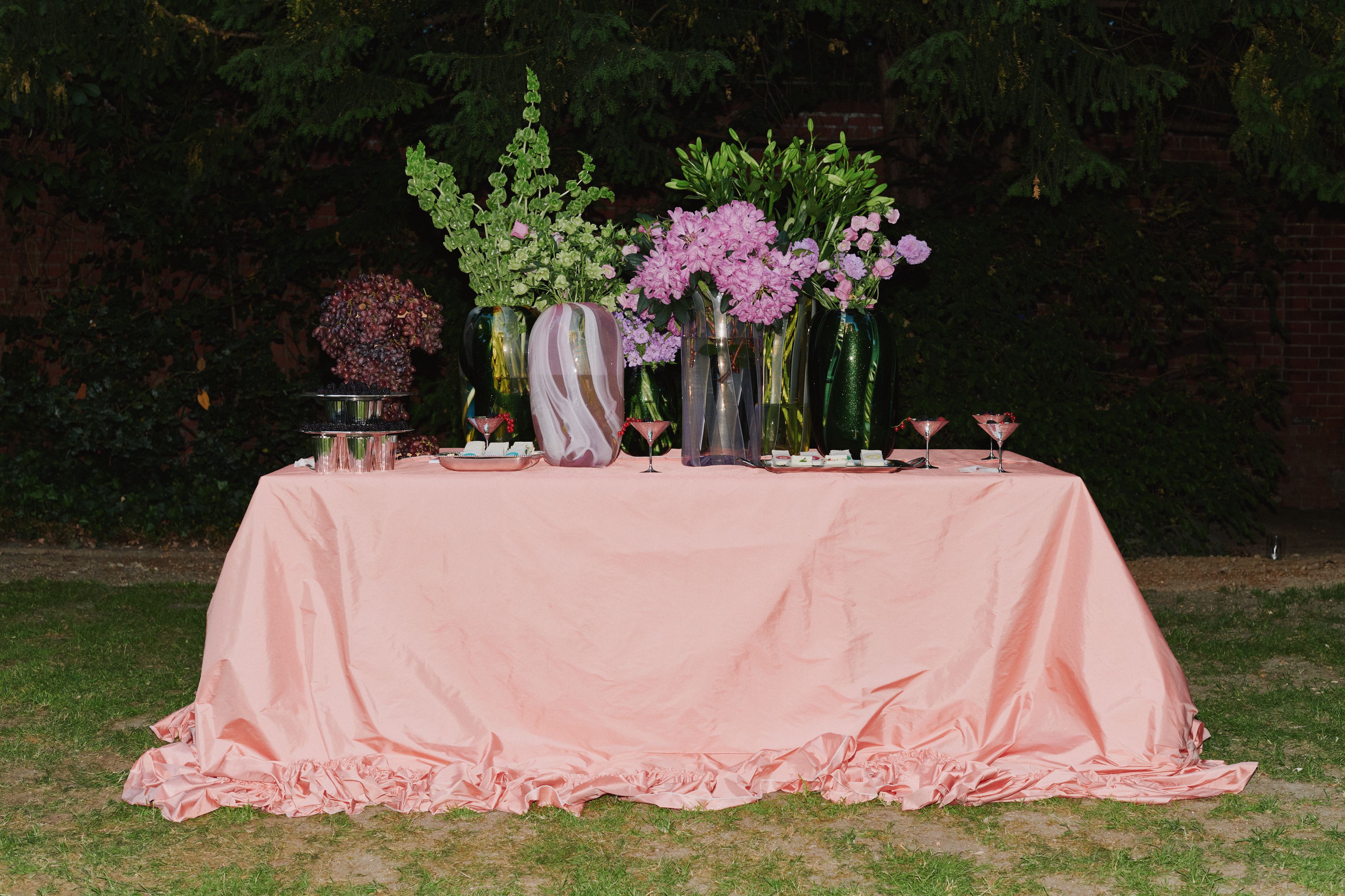 a table in a garden with a tablecloth, vases with lush flowers on top