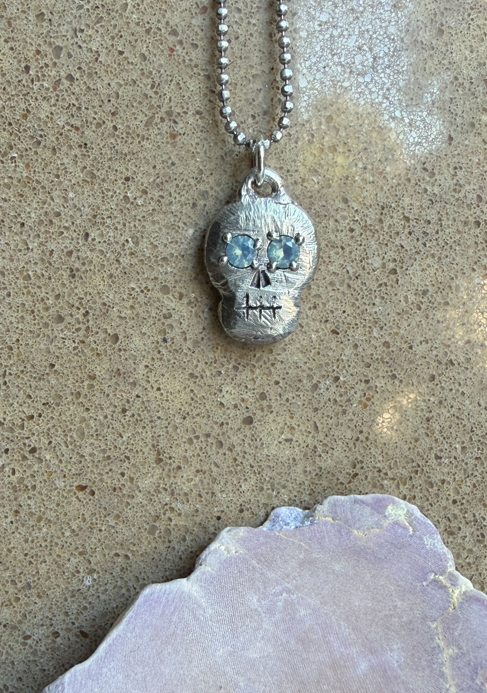 A silver skull pendant with mint green gem eyes