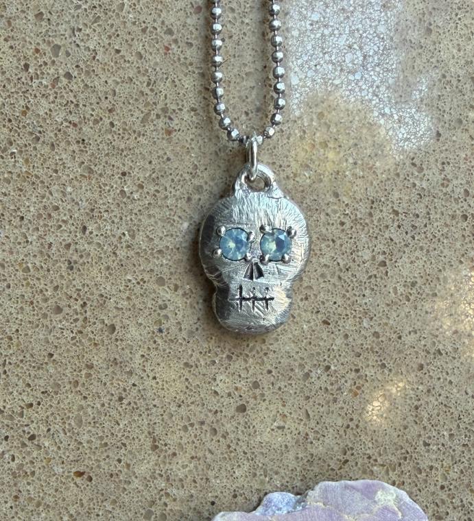 A silver skull pendant with mint green gem eyes