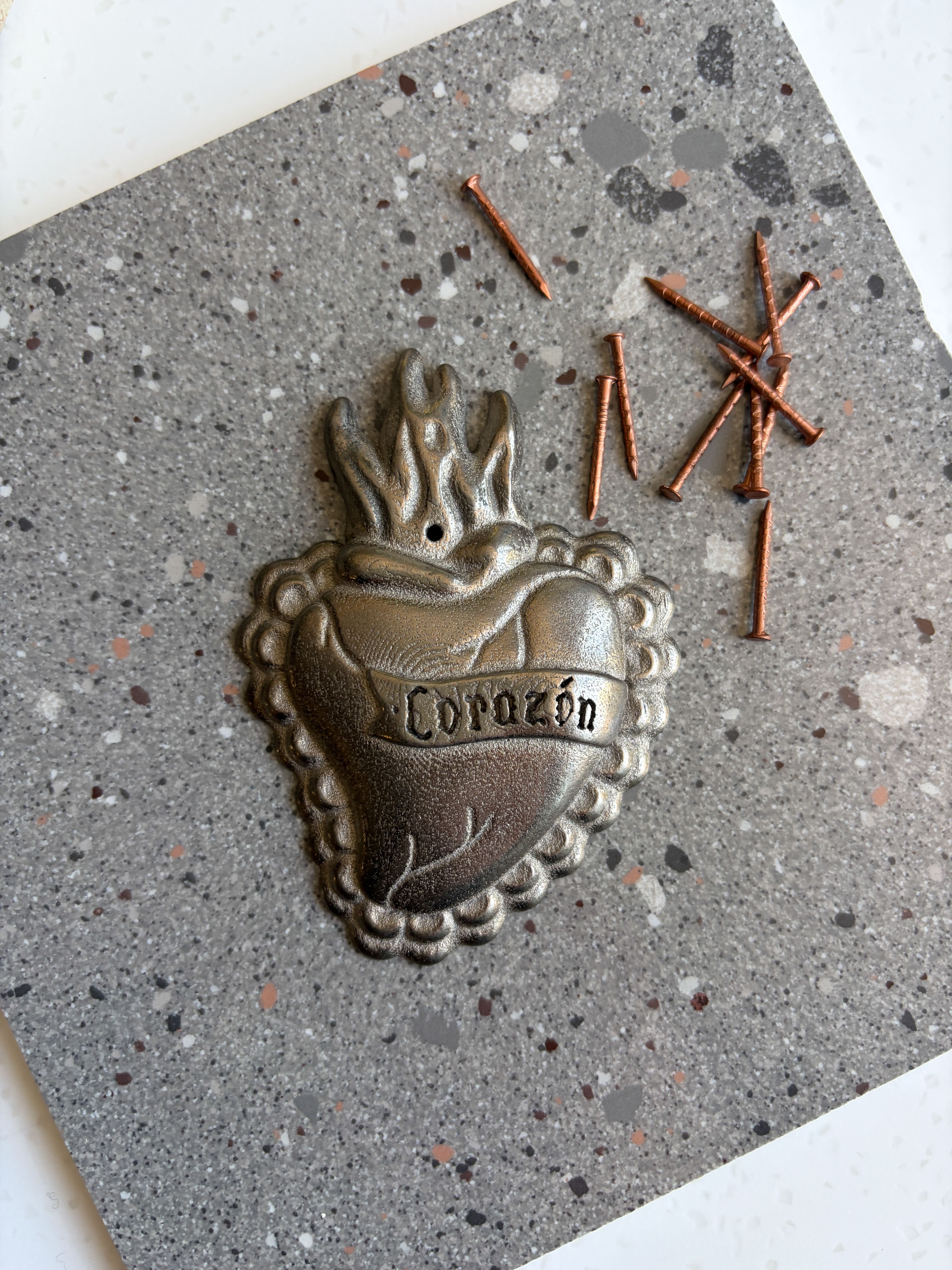 A palm-sized metal burning heart with the word "corazon" written on it.