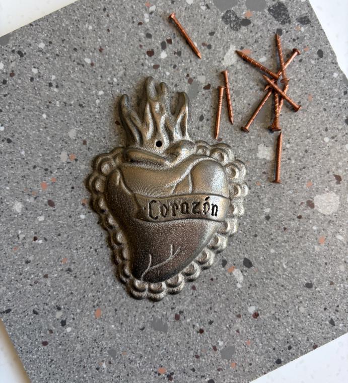 A palm-sized metal burning heart with the word "corazon" written on it.