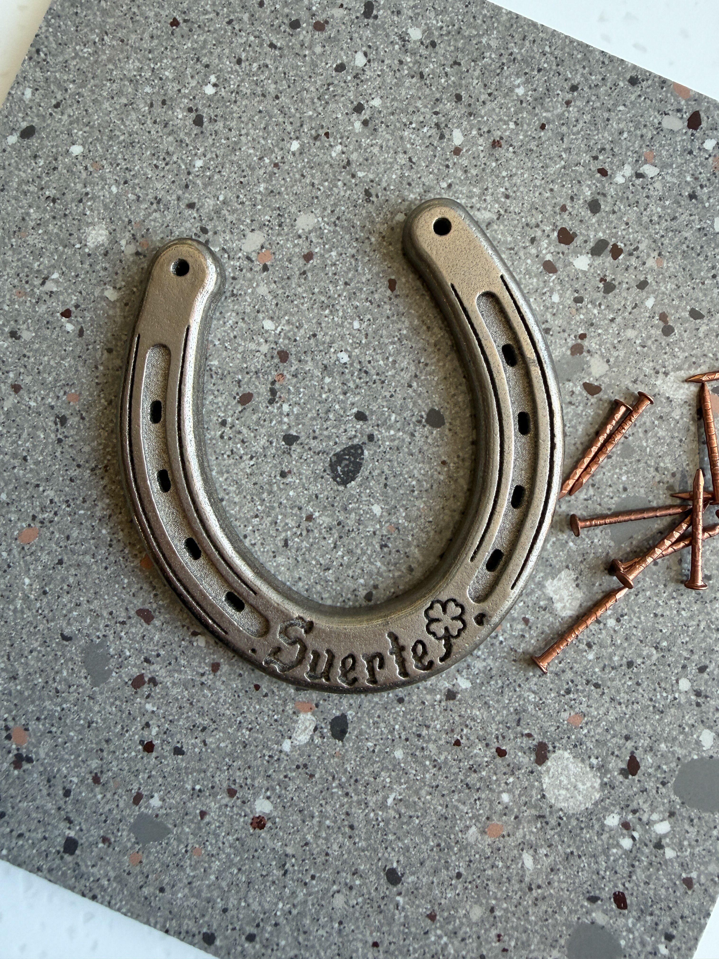 A palm sized metal hose-shoe that reads "Suerte"