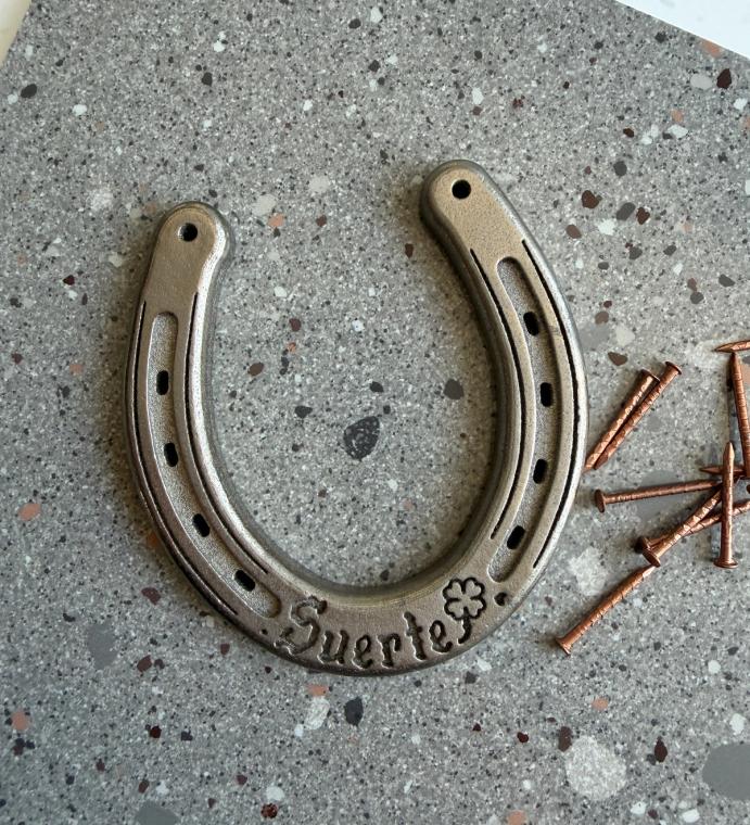 A palm sized metal hose-shoe that reads "Suerte"