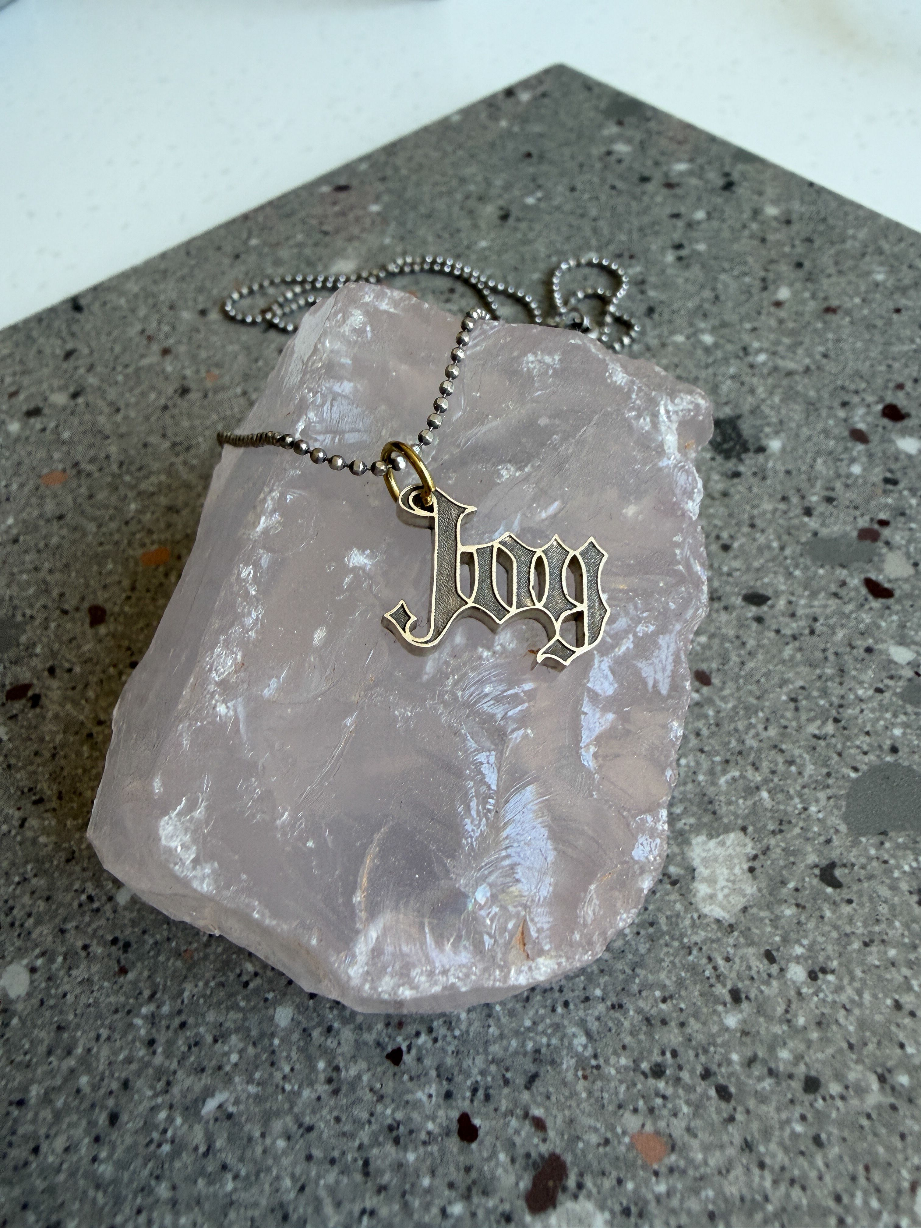 A small pendant that reads "JOY" in a gothic typeface.